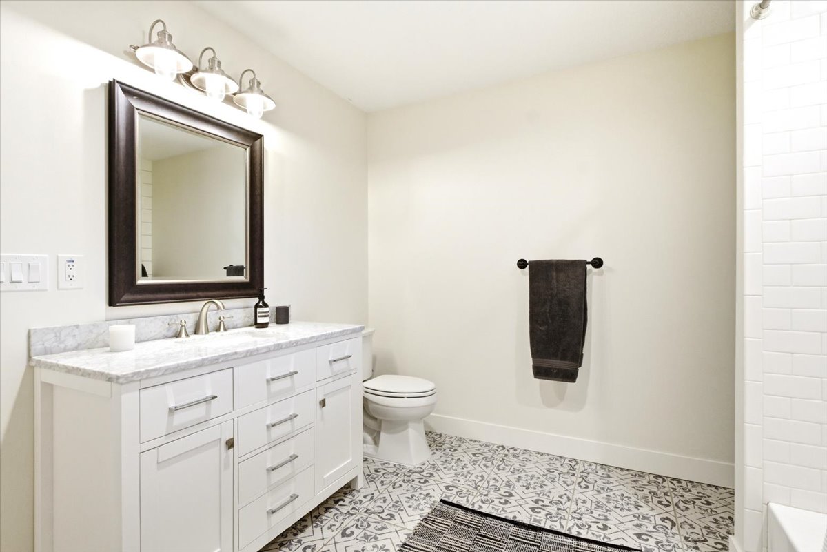 Bathroom featuring a white vanity with a stone countertop, a framed mirror, a three-light vanity fixture, patterned floor tiles, and subway tile shower surround