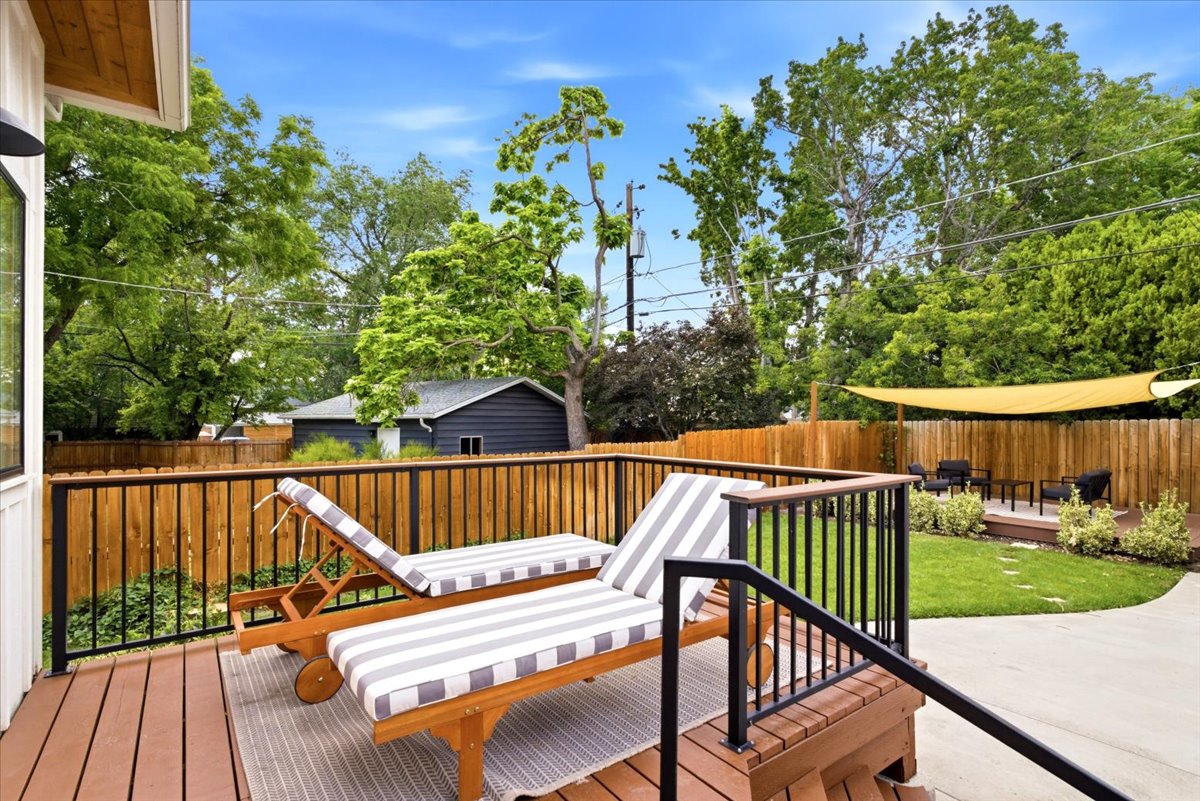 Expansive wood-finish deck with black metal railings, leading to a landscaped lawn