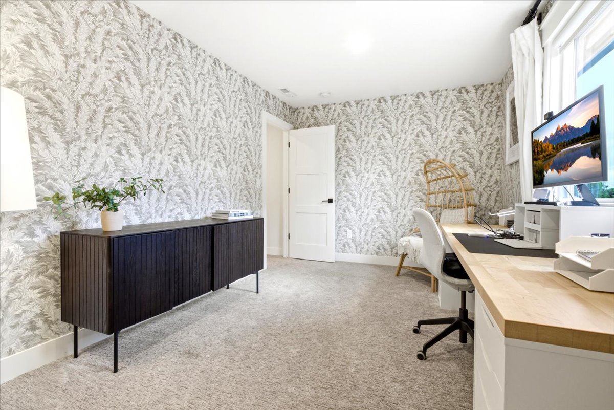 Room featuring patterned wall covering, neutral carpet flooring, and a window with white drapes