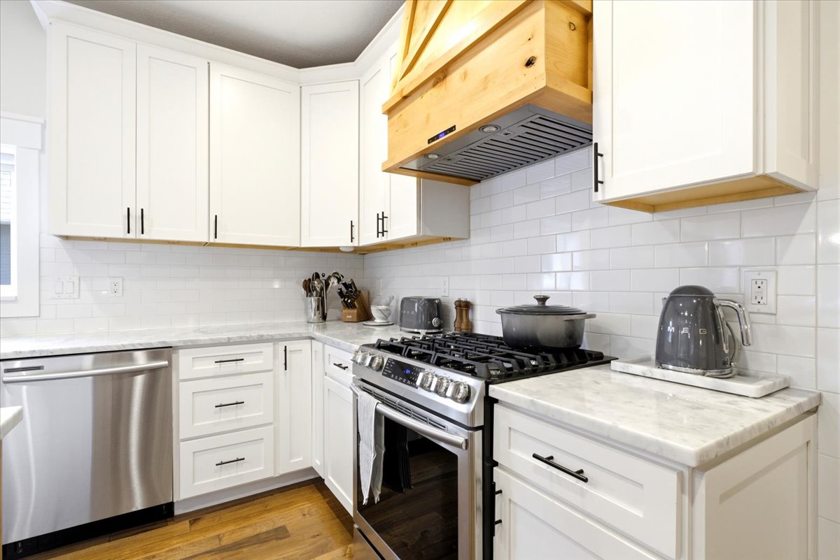 Modern kitchen featuring white shaker cabinetry, stainless steel appliances, a subway tile backsplash, light-toned countertops, and wood-finish flooring