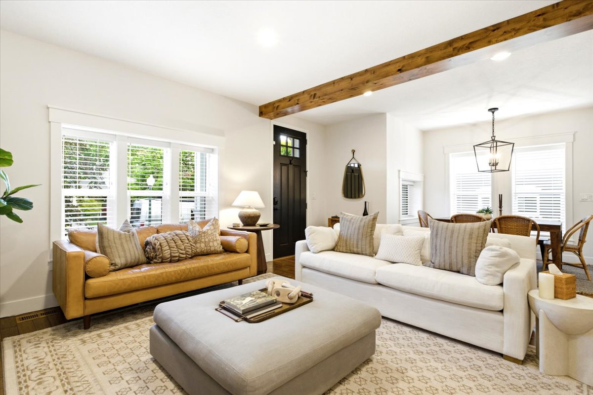 Open-concept living area featuring a decorative wood beam, white walls, and wood-finish flooring