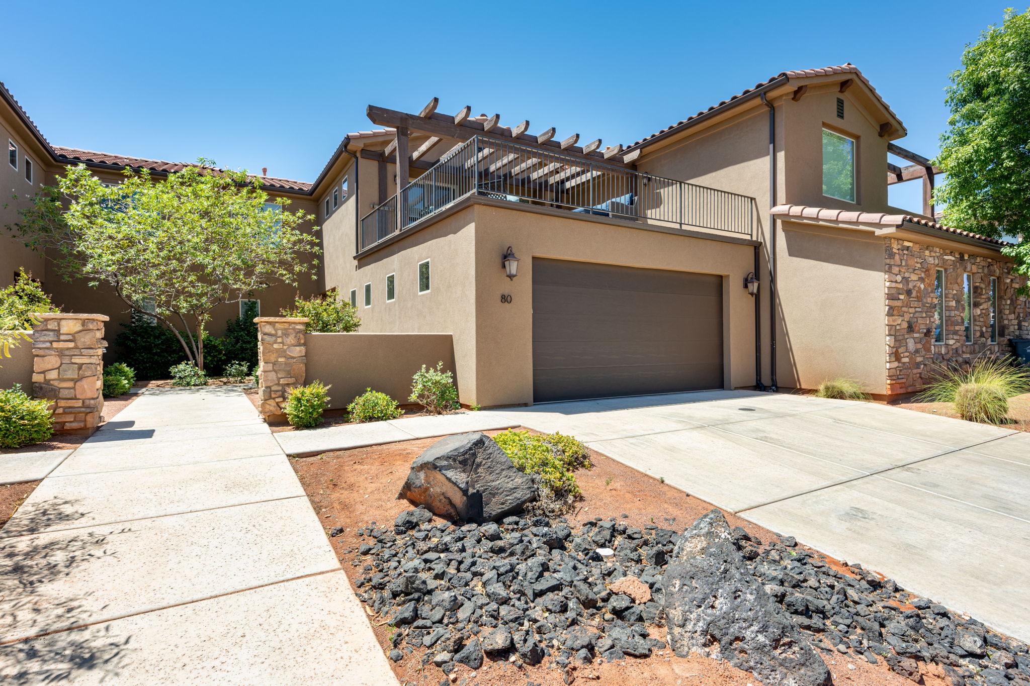 Stucco exterior featuring a two-car garage, stone accents, and an upper-level patio with a pergola