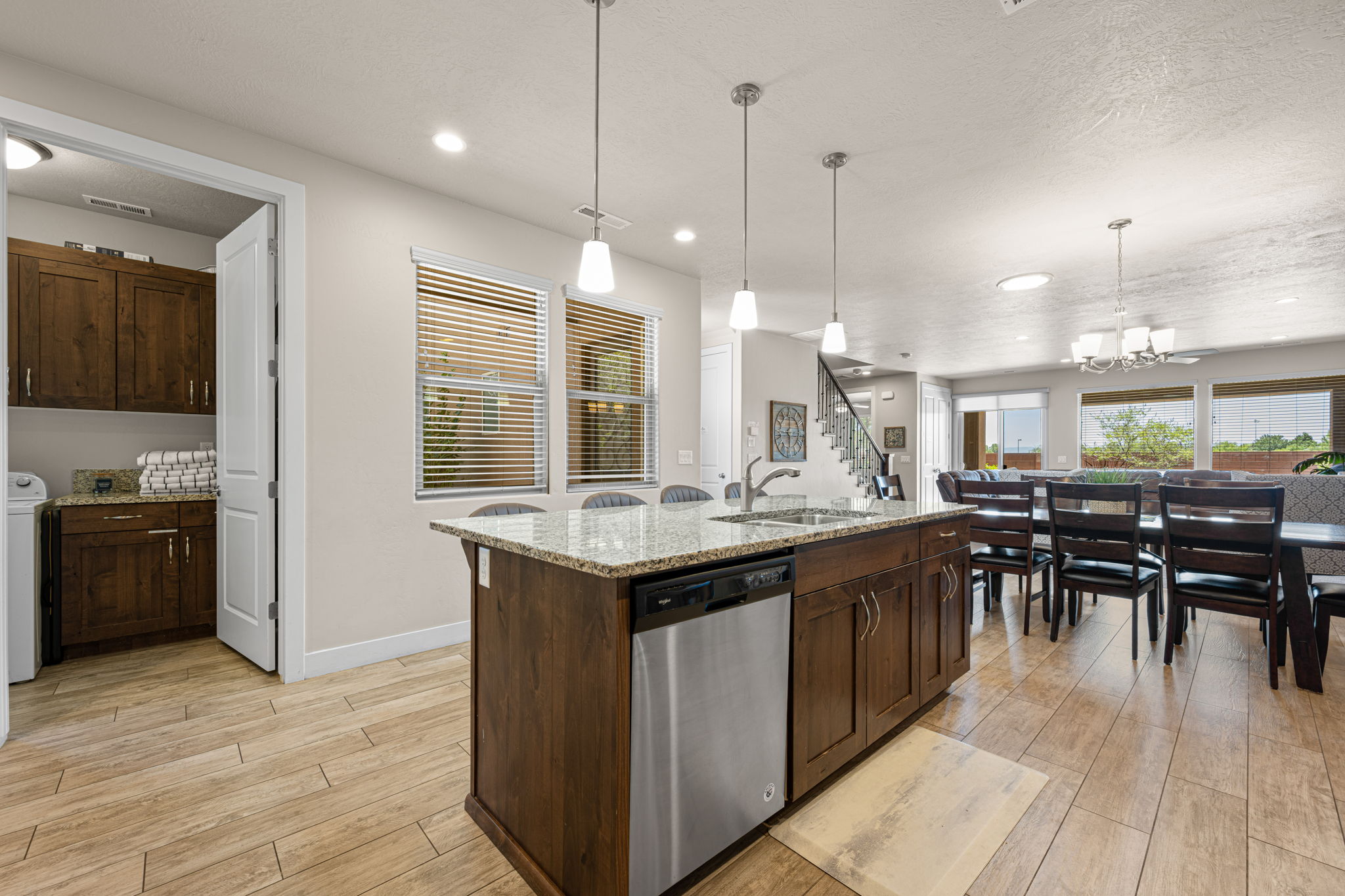 Open-concept kitchen featuring a large island with sink, stainless steel dishwasher, pendant lighting, and wood-finish flooring