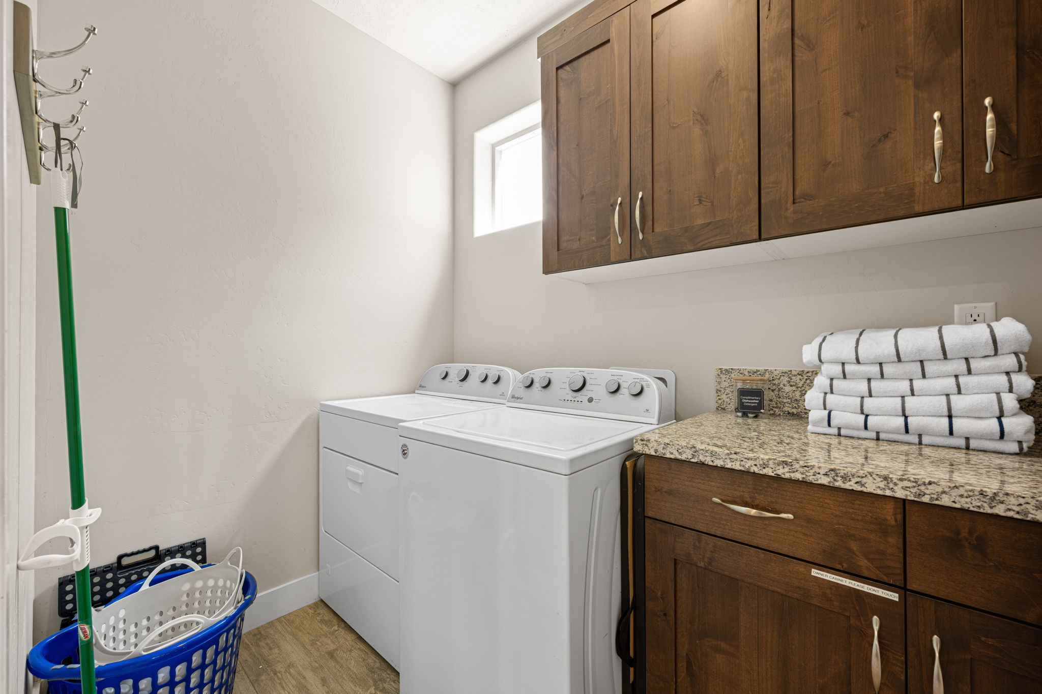 Dedicated laundry area featuring wood-finish flooring, upper and lower wood cabinetry with decorative hardware, and a granite countertop