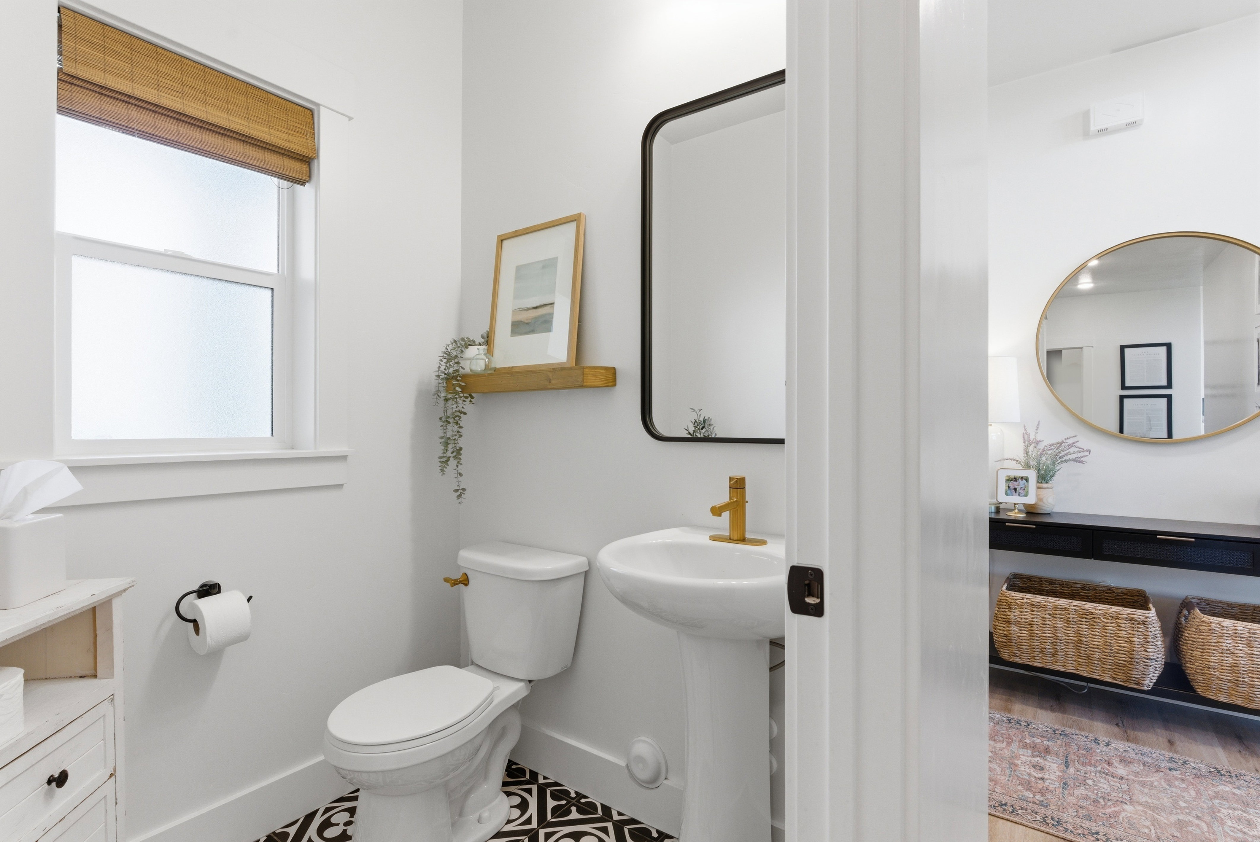 Pedestal sink with gold-finish faucet, black-frame mirror, and patterned floor tile