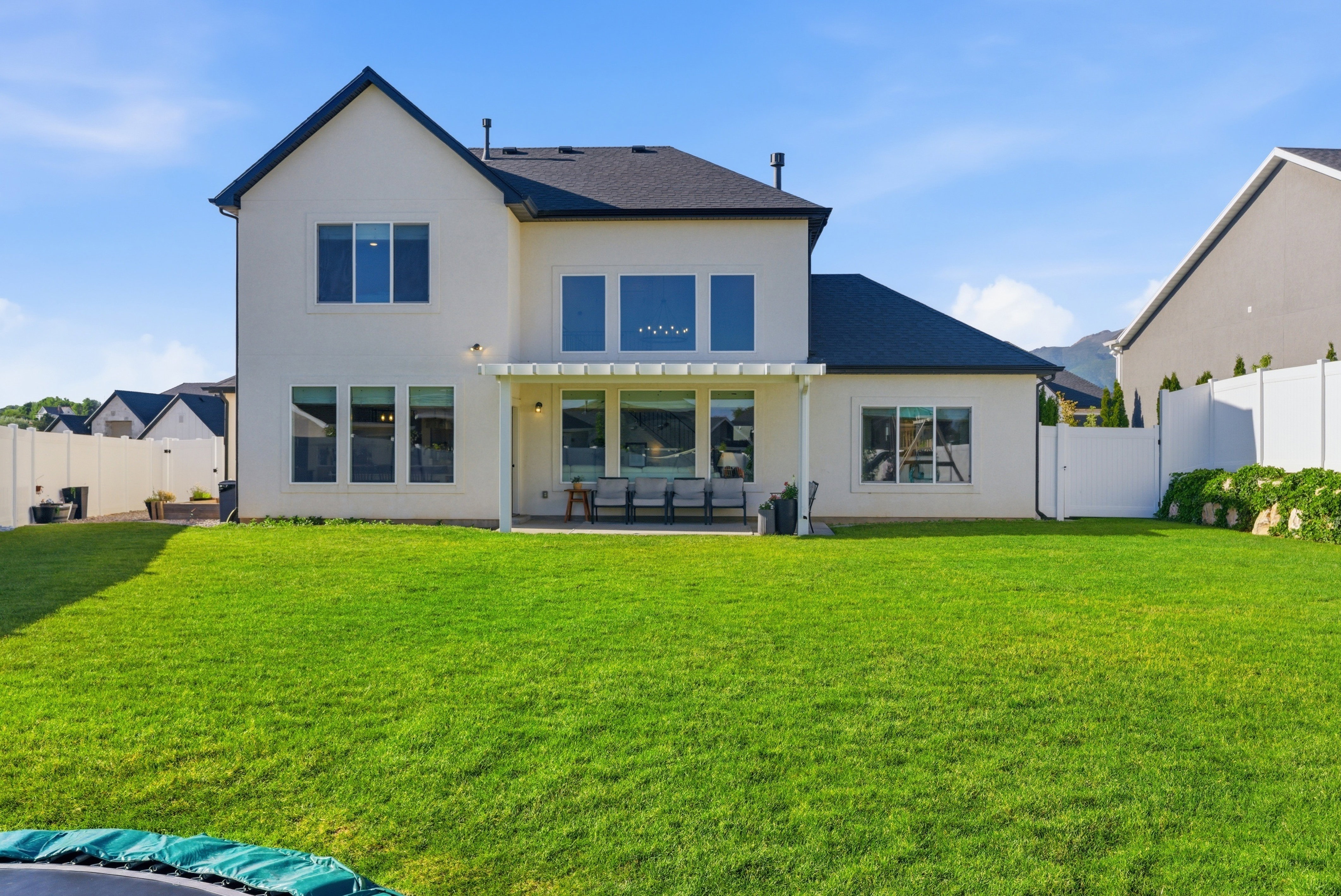 Expansive backyard featuring a lush green lawn, full privacy fencing, and a covered patio area