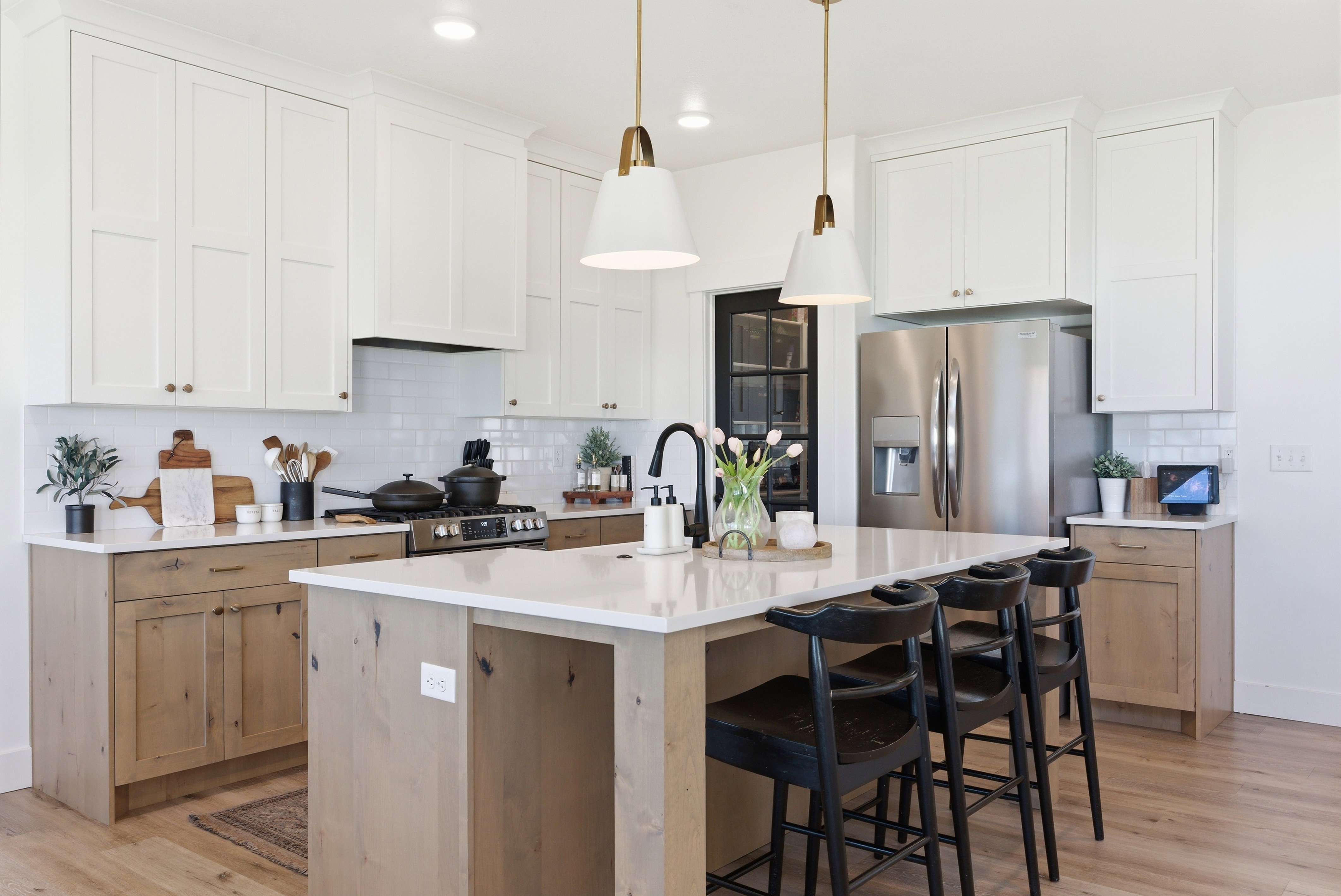 Modern kitchen featuring a central island with countertop seating, two-tone cabinetry with white upper and wood-finish lower cabinets, stainless steel appliances, a subway tile backsplash, and recessed lighting with pendant fixtures