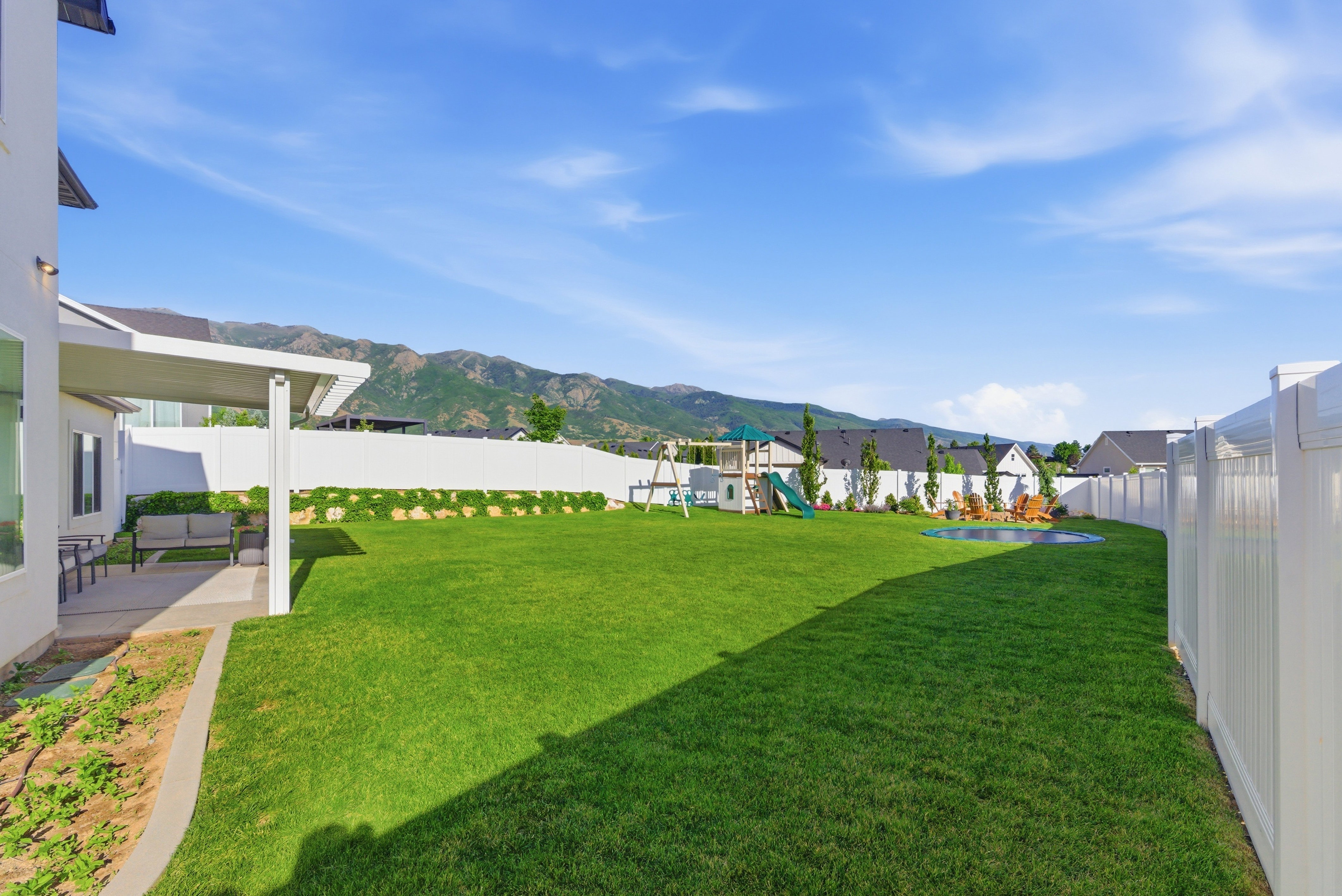 Expansive backyard featuring a lush lawn, white vinyl fencing, and a covered patio area