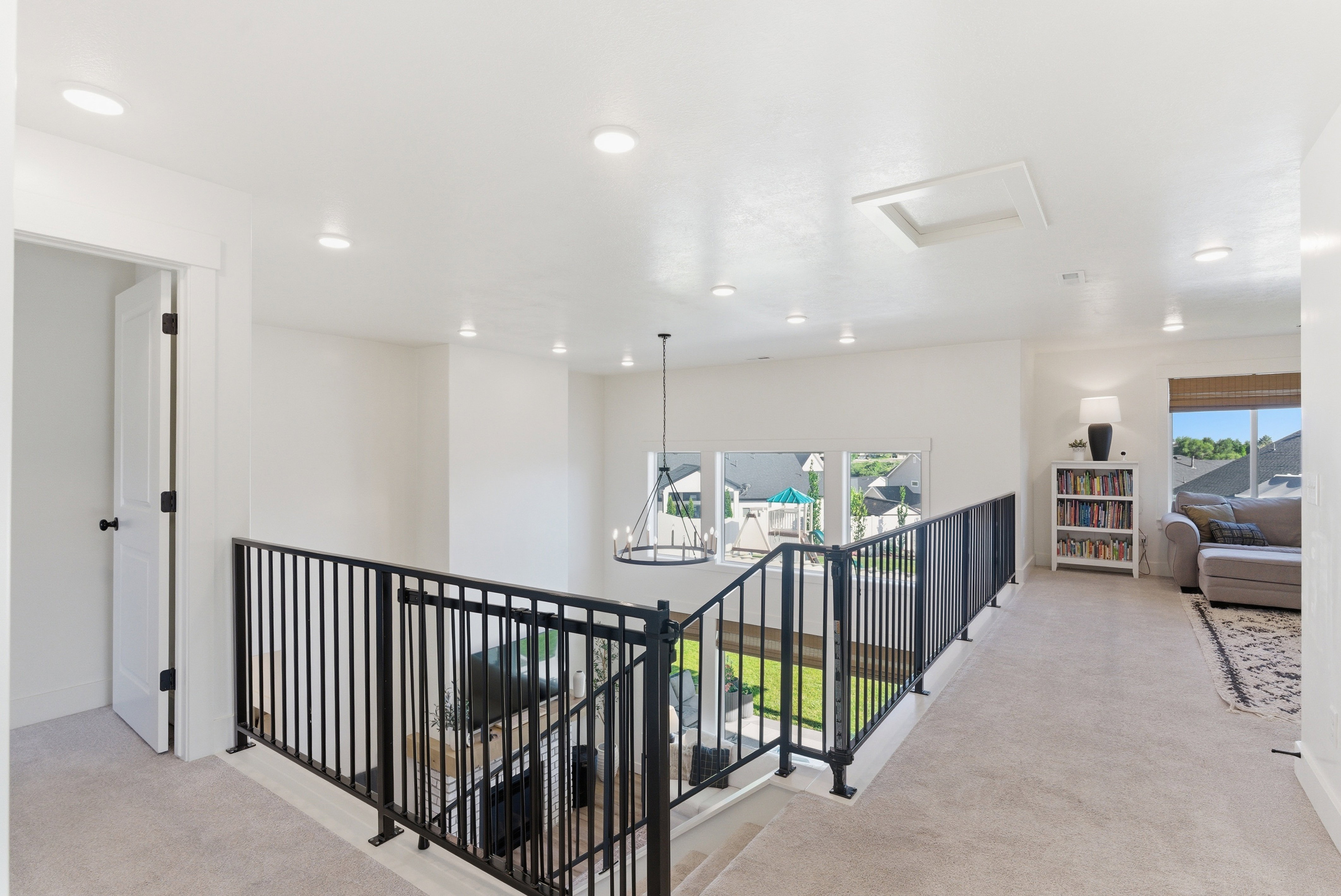 Upper-level landing featuring light-colored carpeting, recessed ceiling lights, and a black wrought iron railing overlooking a lower space