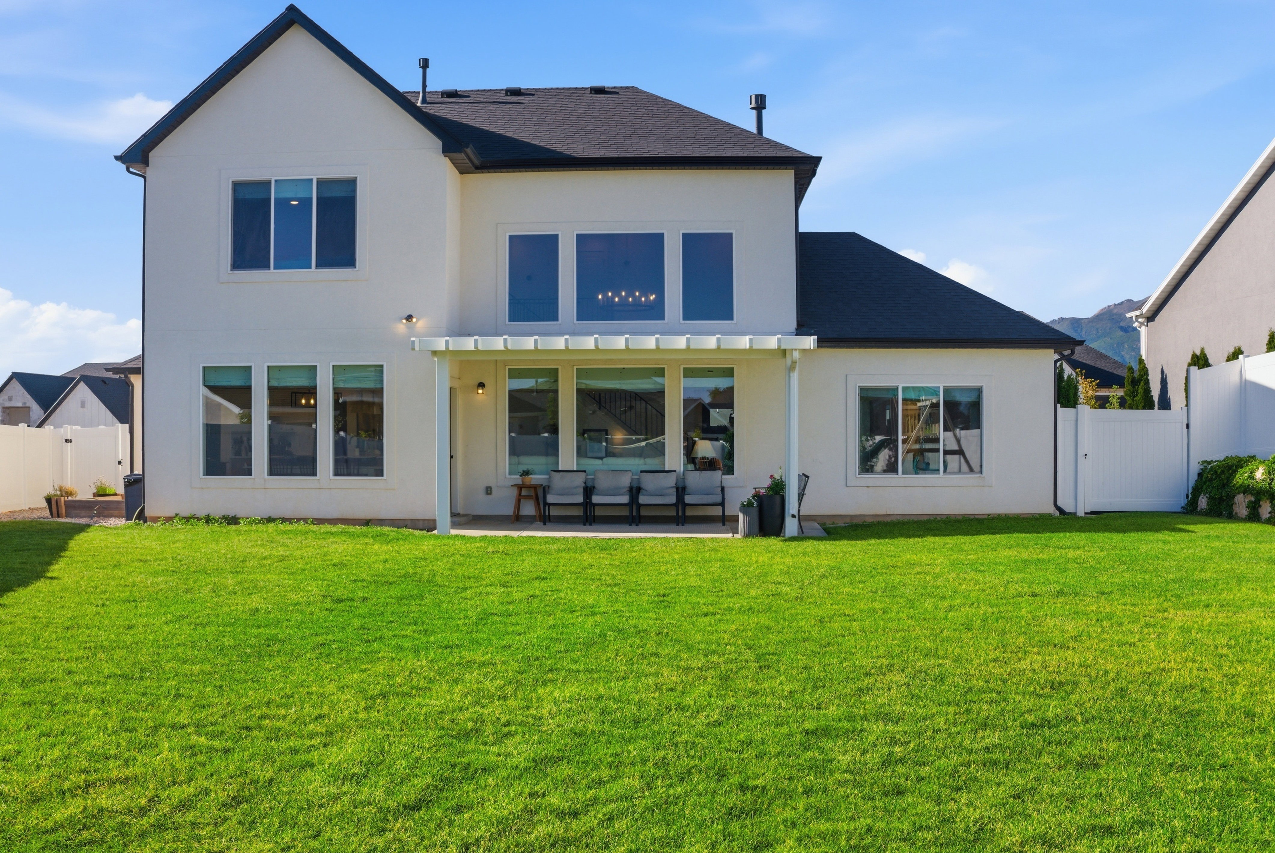 Expansive backyard with a manicured lawn, a covered patio area, and a white privacy fence