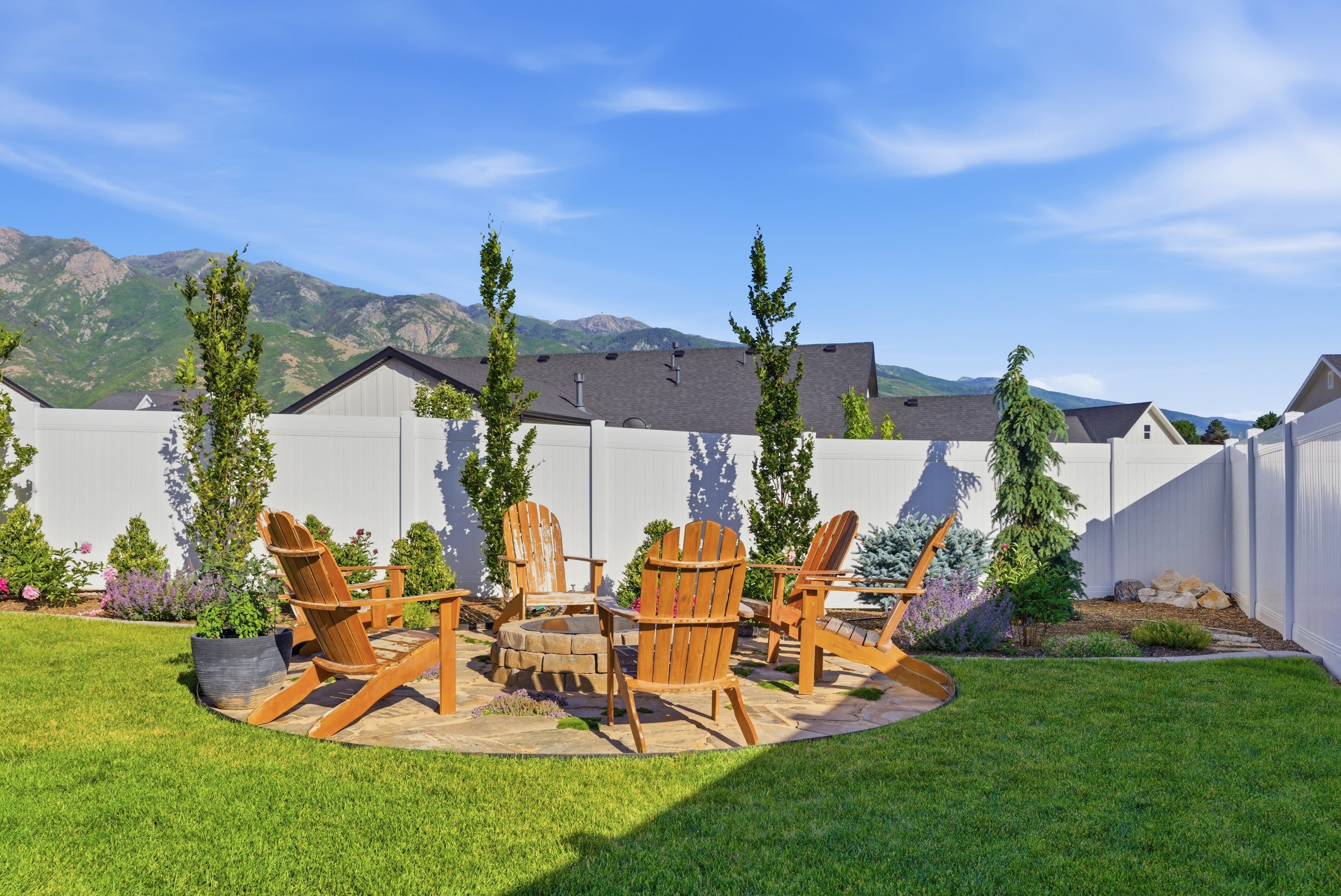 Expansive backyard featuring a circular stone patio, integrated fire pit, and surrounding garden beds with mature trees