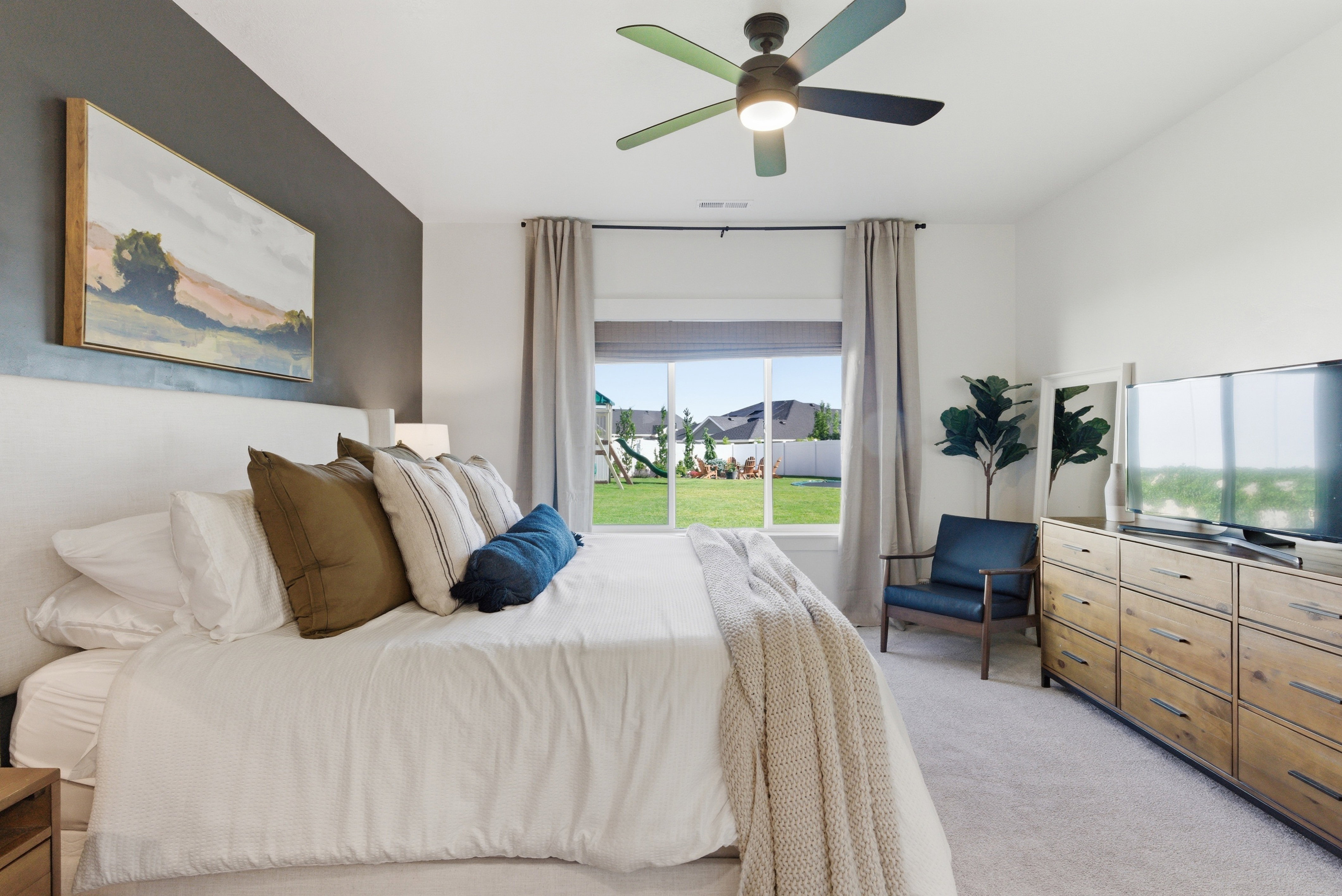 Carpeted room with a large window, a ceiling fan with integrated lighting, and a dark accent wall