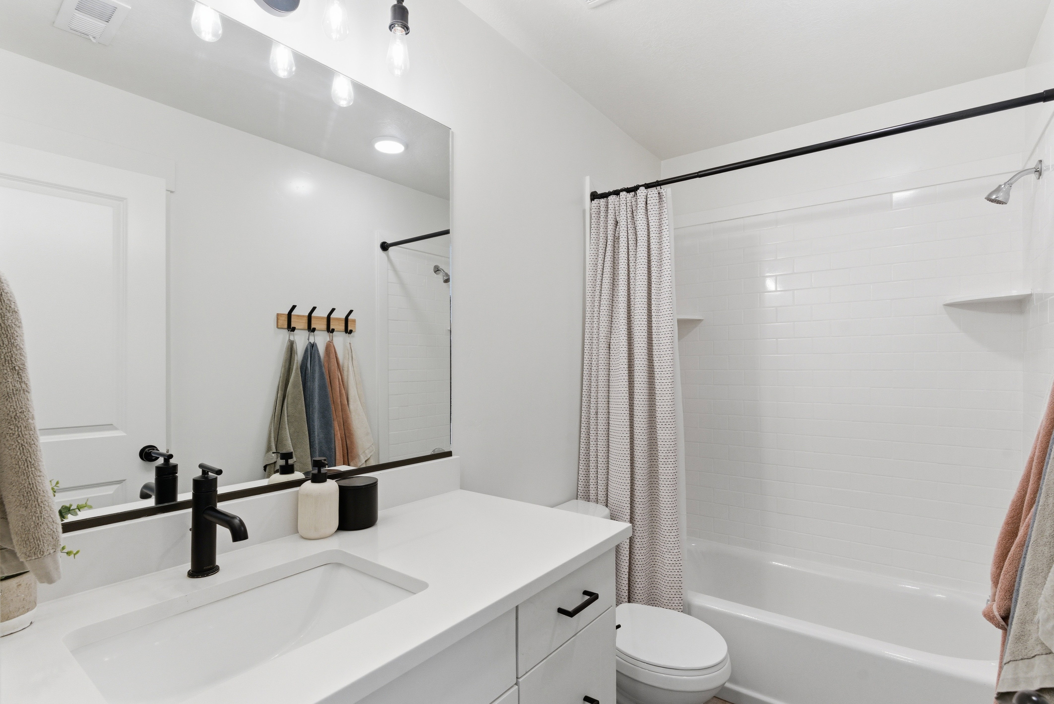 Bathroom featuring a built-in vanity with an integrated sink and matte black faucet, a large wall mirror with overhead lighting, and a bathtub with subway tile surround
