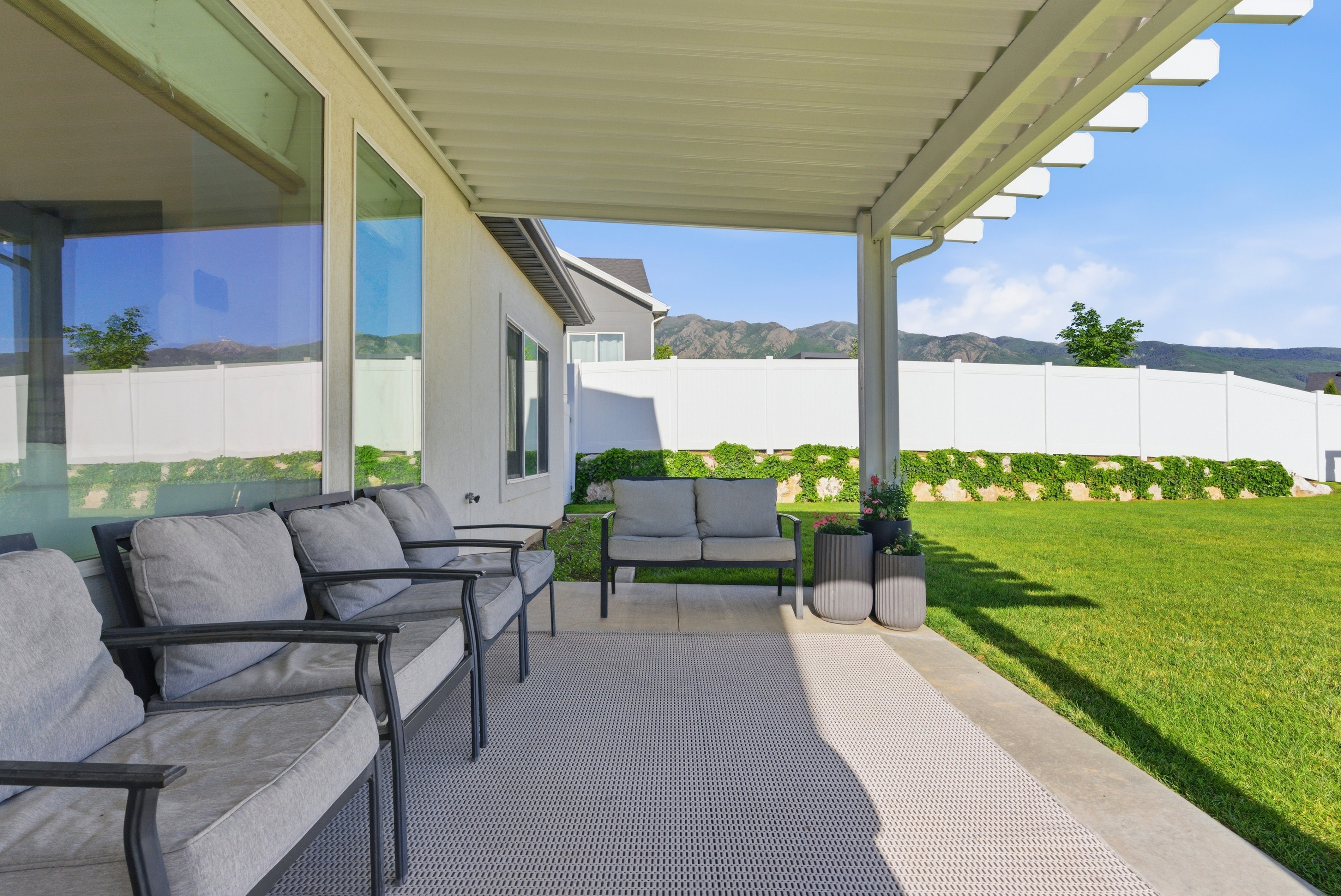 Expansive covered patio featuring a solid roof structure with open pergola details, a concrete slab base, and direct access to a large, well-maintained lawn