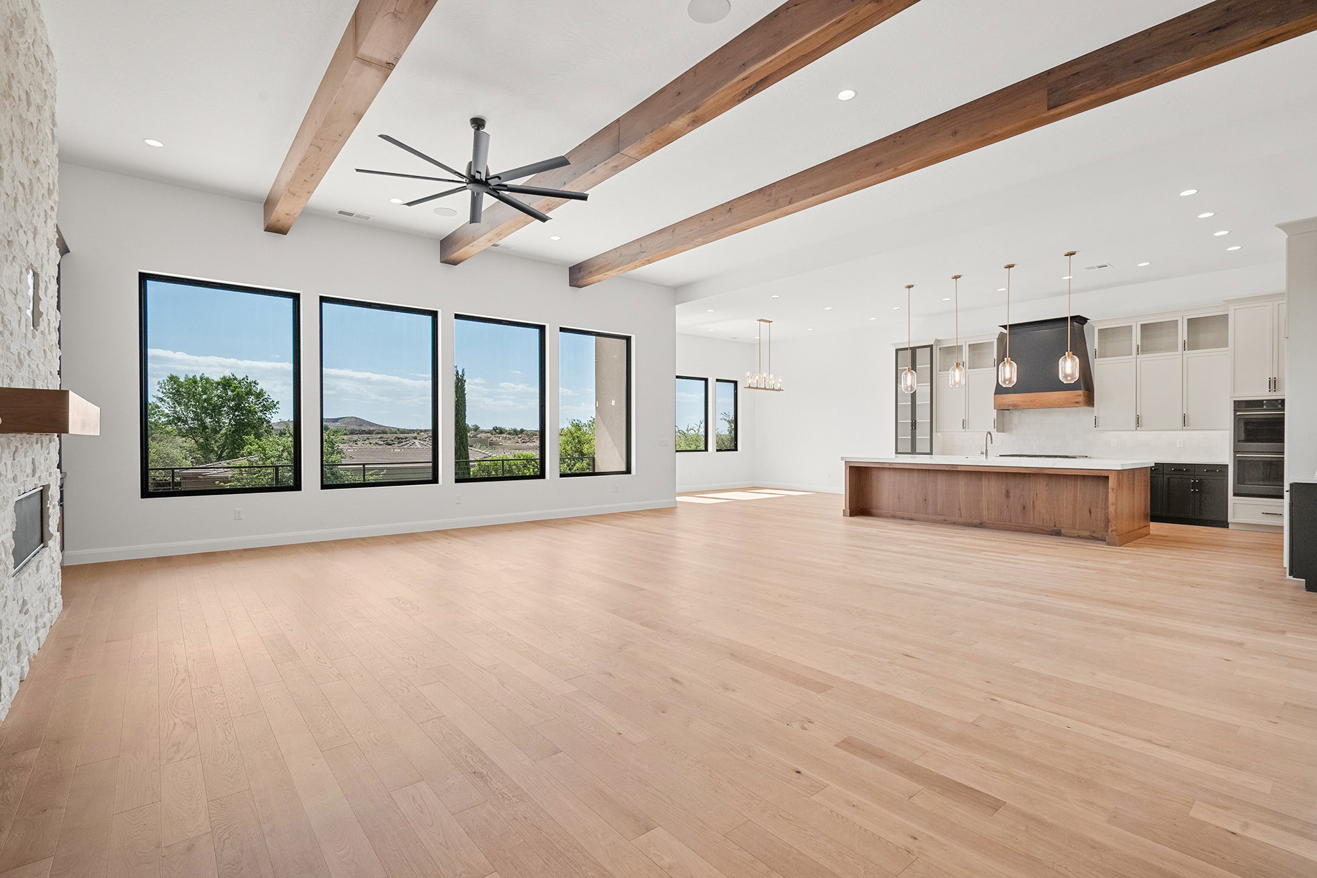 Spacious open-concept living area featuring light wood-finish flooring, exposed wood ceiling beams, and a fireplace with a stone surround