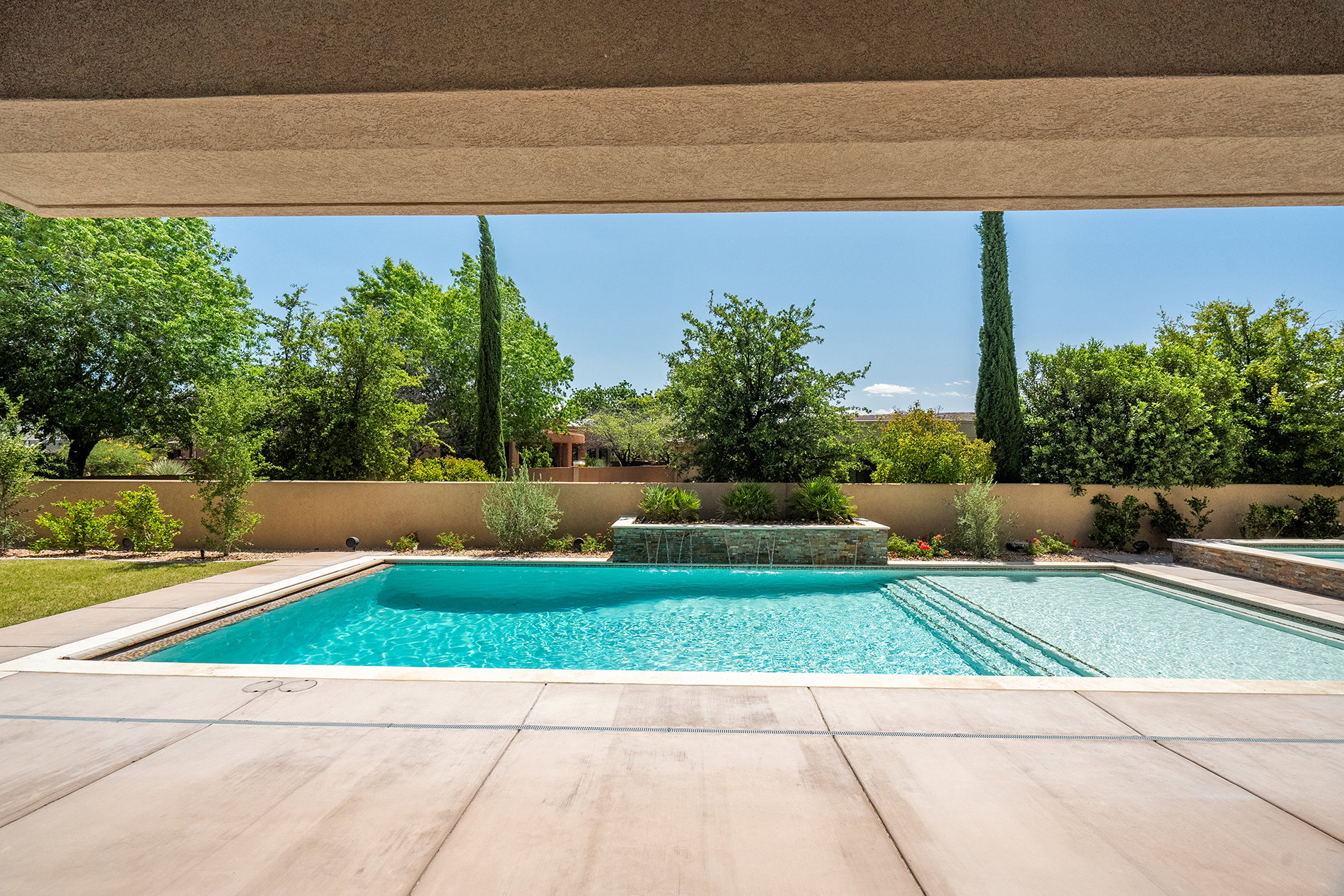 Expansive outdoor living area featuring a multi-level swimming pool with integrated spa and waterfall feature, surrounded by concrete decking