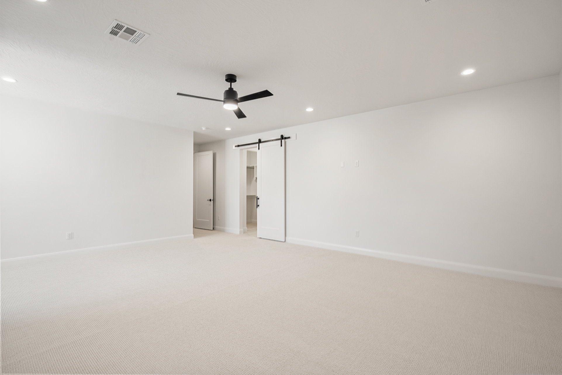 Spacious room featuring neutral carpeting, white walls, recessed ceiling lighting, a contemporary ceiling fan, and a barn door entry to a closet with shelving