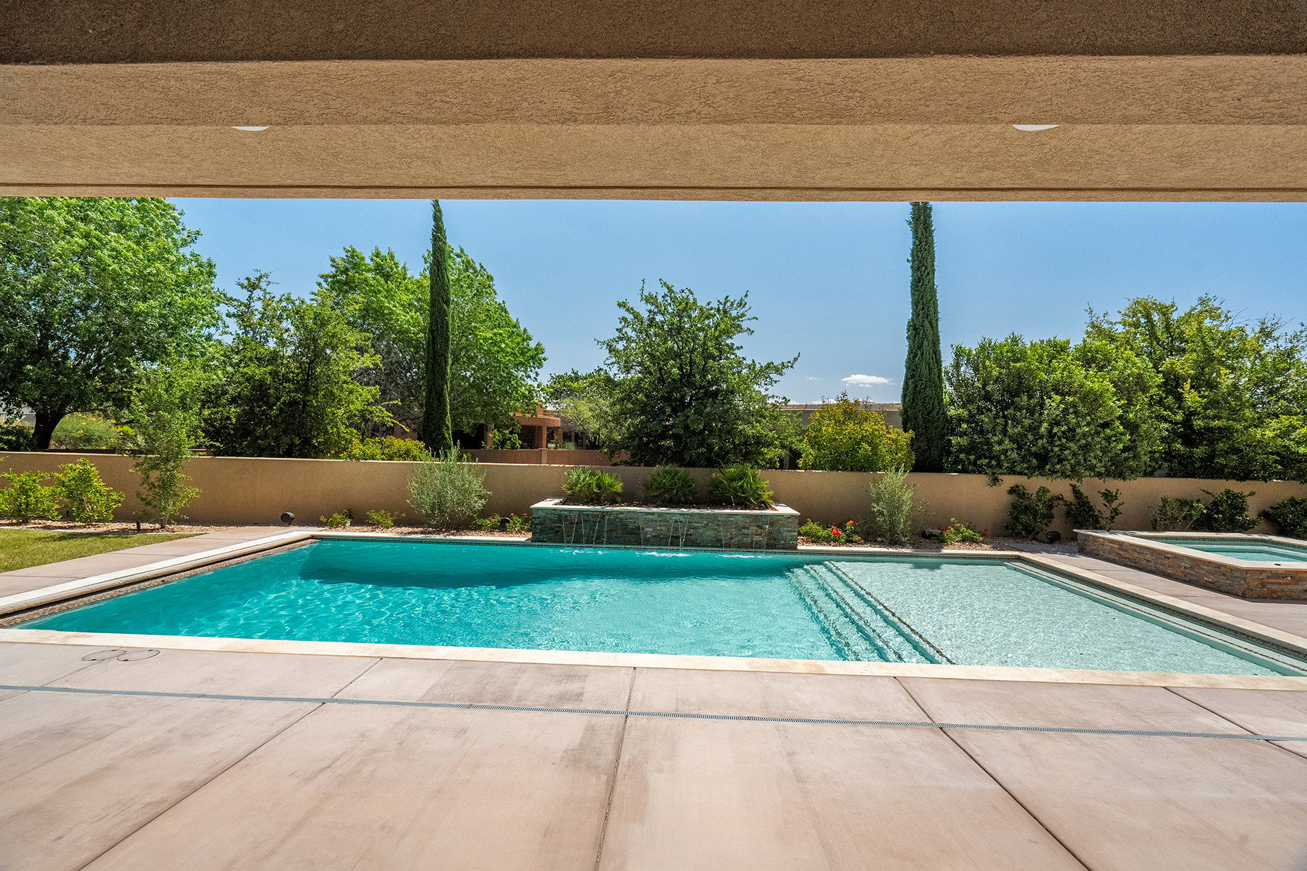 Outdoor living space featuring a swimming pool with integrated steps, an adjacent spa, and a stone-faced water feature