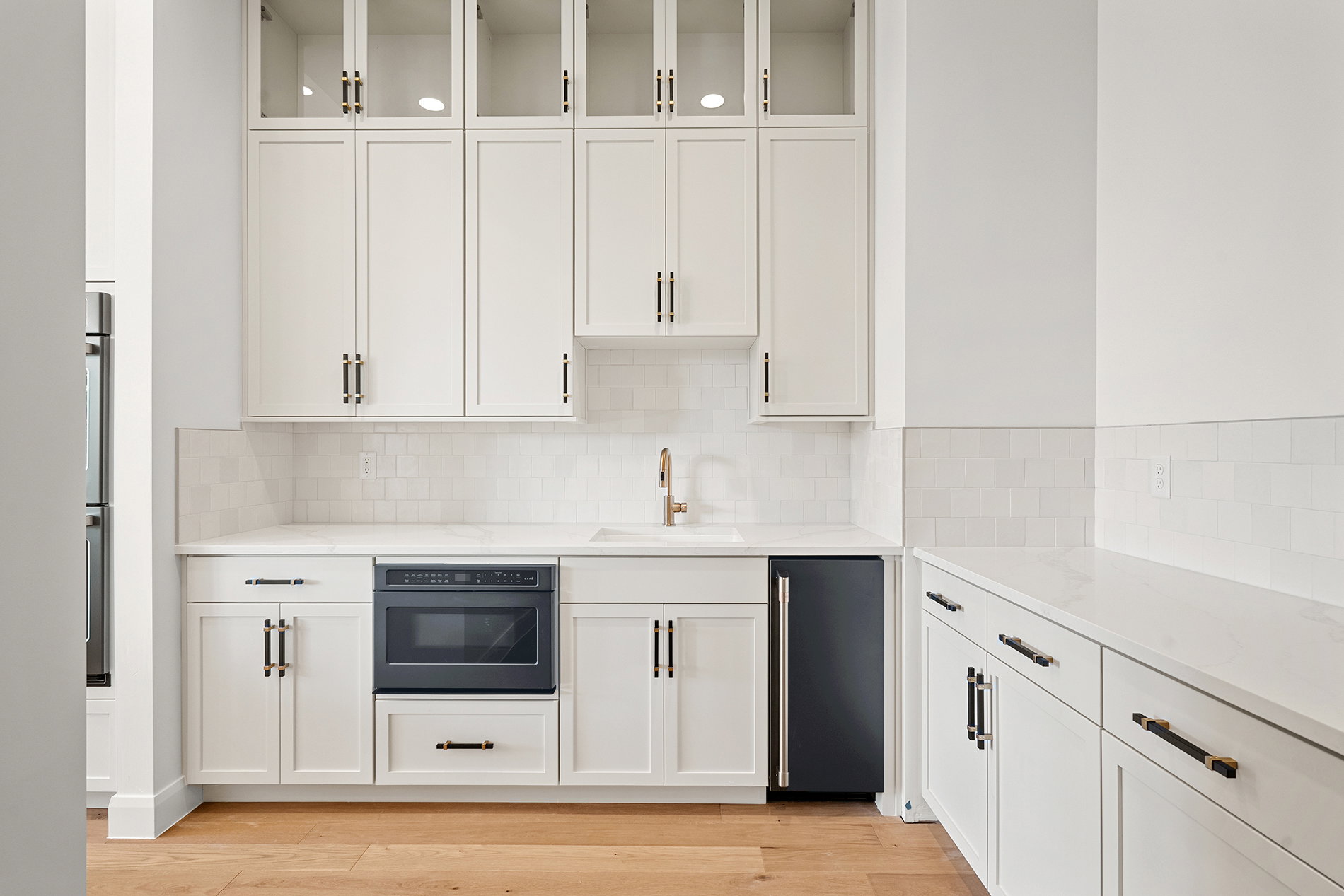 Built-in wet bar featuring white shaker cabinetry, glass-front upper cabinets, a subway tile backsplash, and light-toned countertops