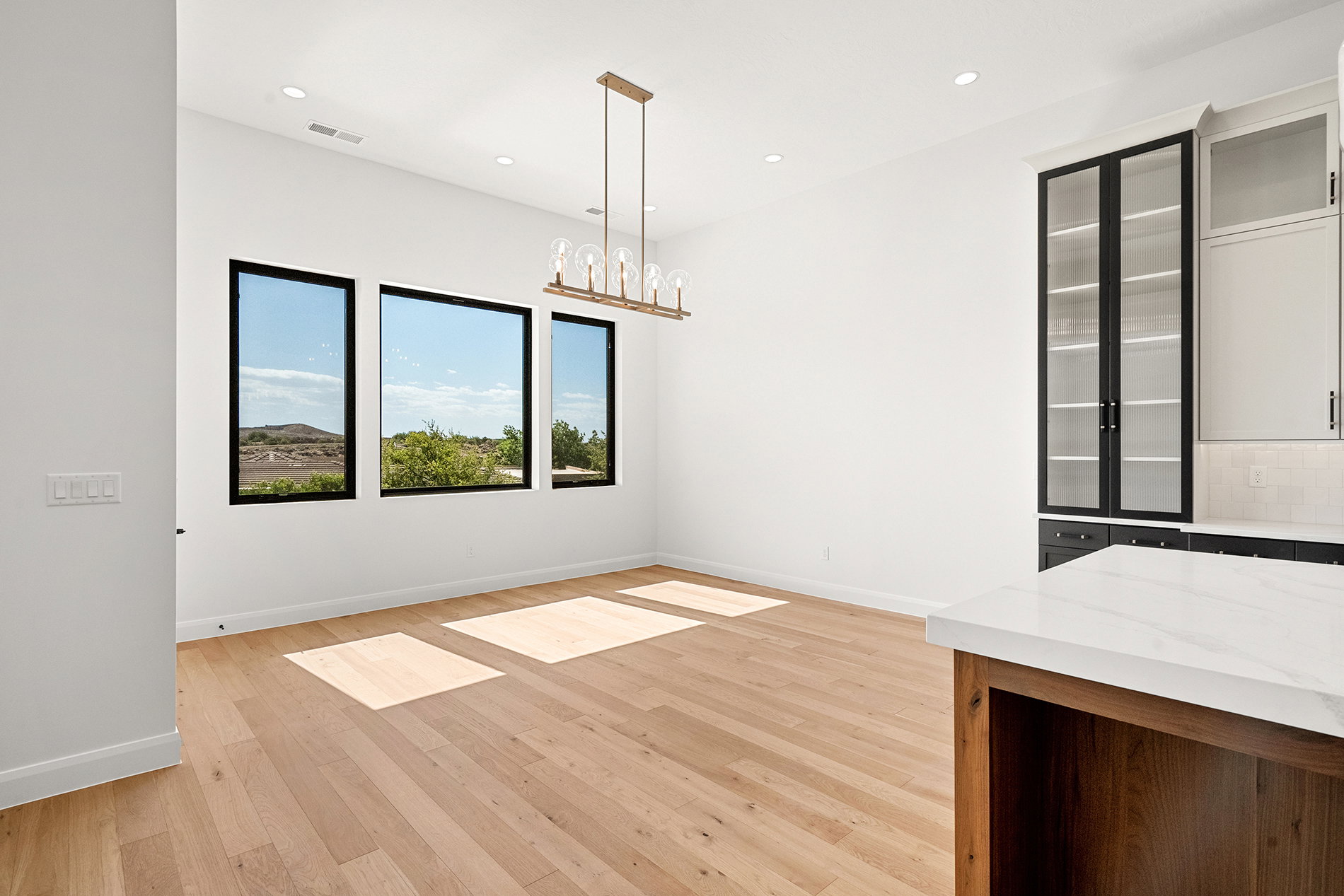 Spacious interior featuring wood-finish flooring, ample natural light from three large windows, and a contemporary linear chandelier