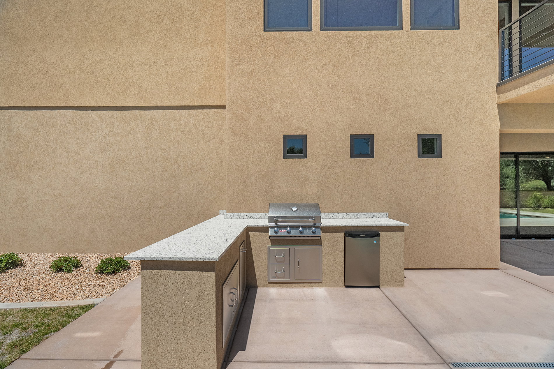 Outdoor kitchen featuring a built-in stainless steel grill, integrated under-counter refrigerator, and ample counter space with a light-toned, speckled finish
