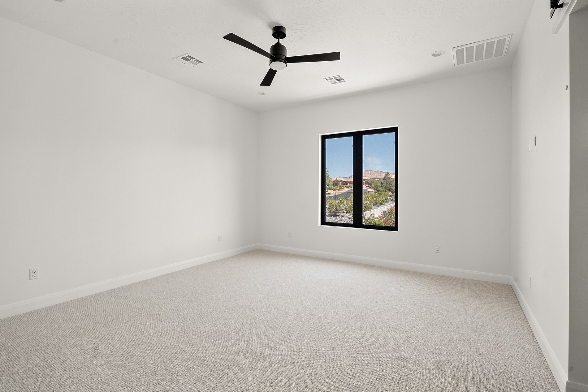 Spacious room featuring light-colored carpet flooring, a modern black ceiling fan, and recessed lighting