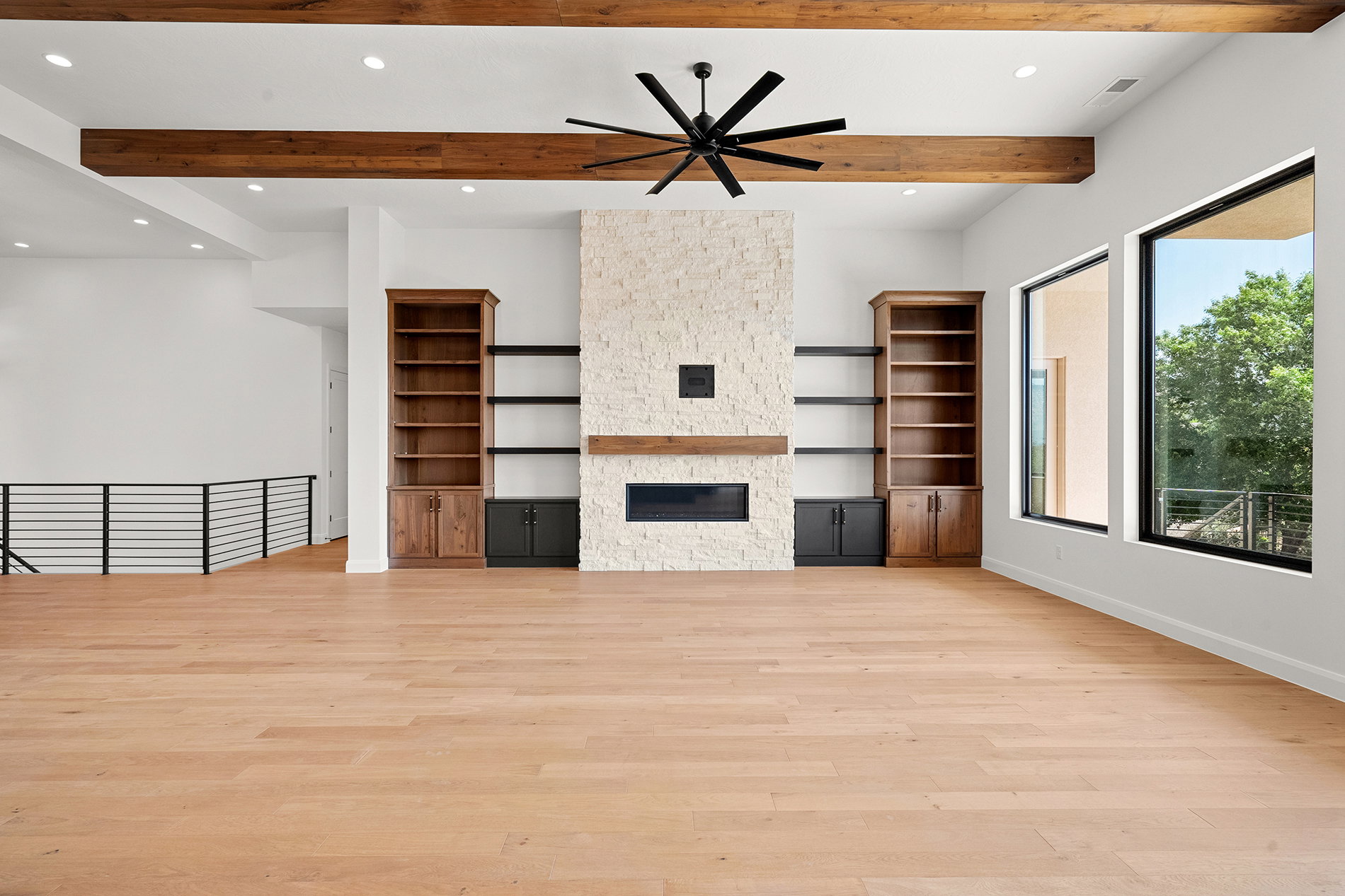Spacious living area featuring high ceilings with exposed wood beams, a stone-clad fireplace with a wood mantel, and built-in shelving units