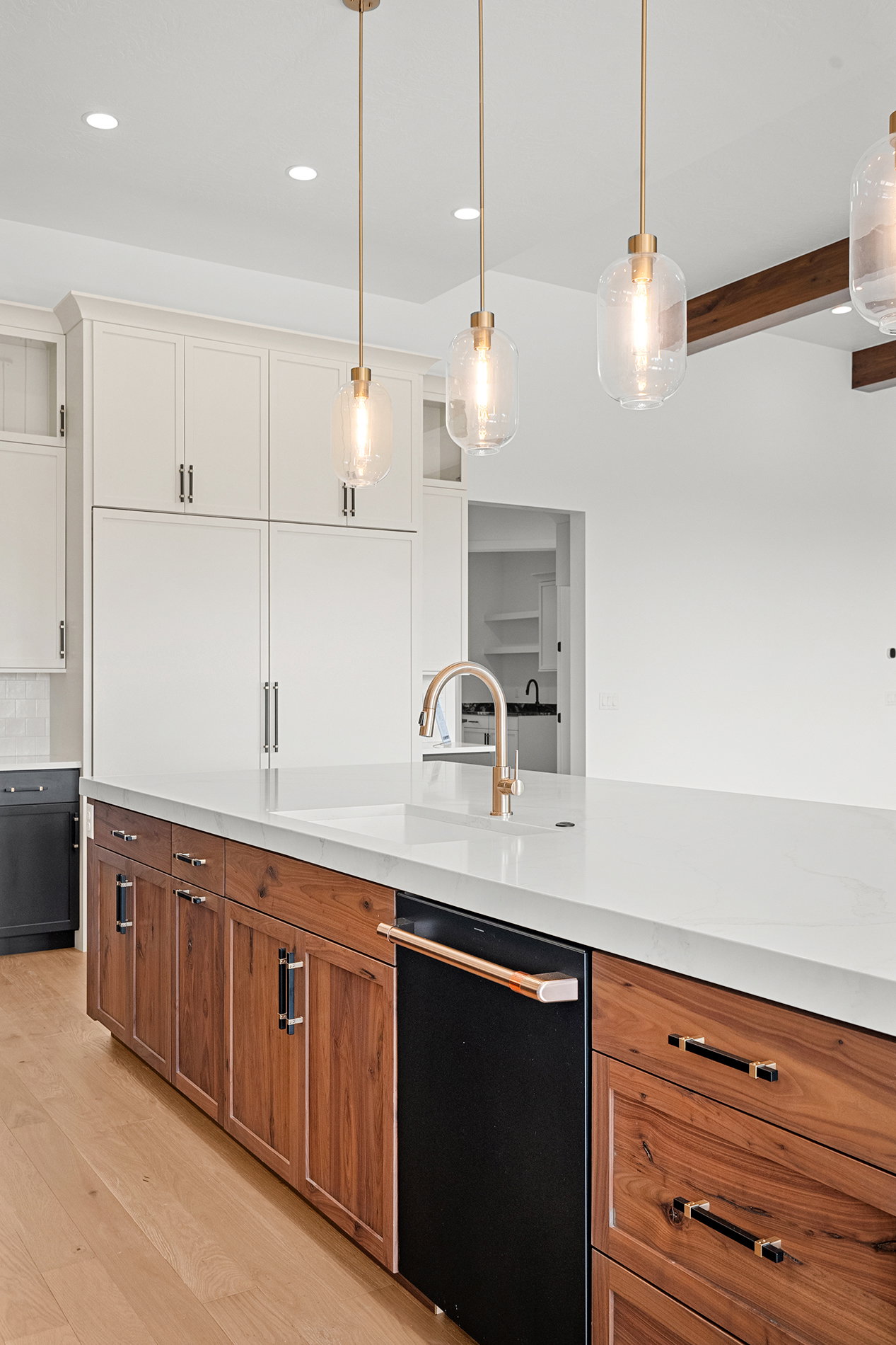 Kitchen island featuring a white countertop, integrated sink with a gold-tone faucet, and wood-finish cabinetry