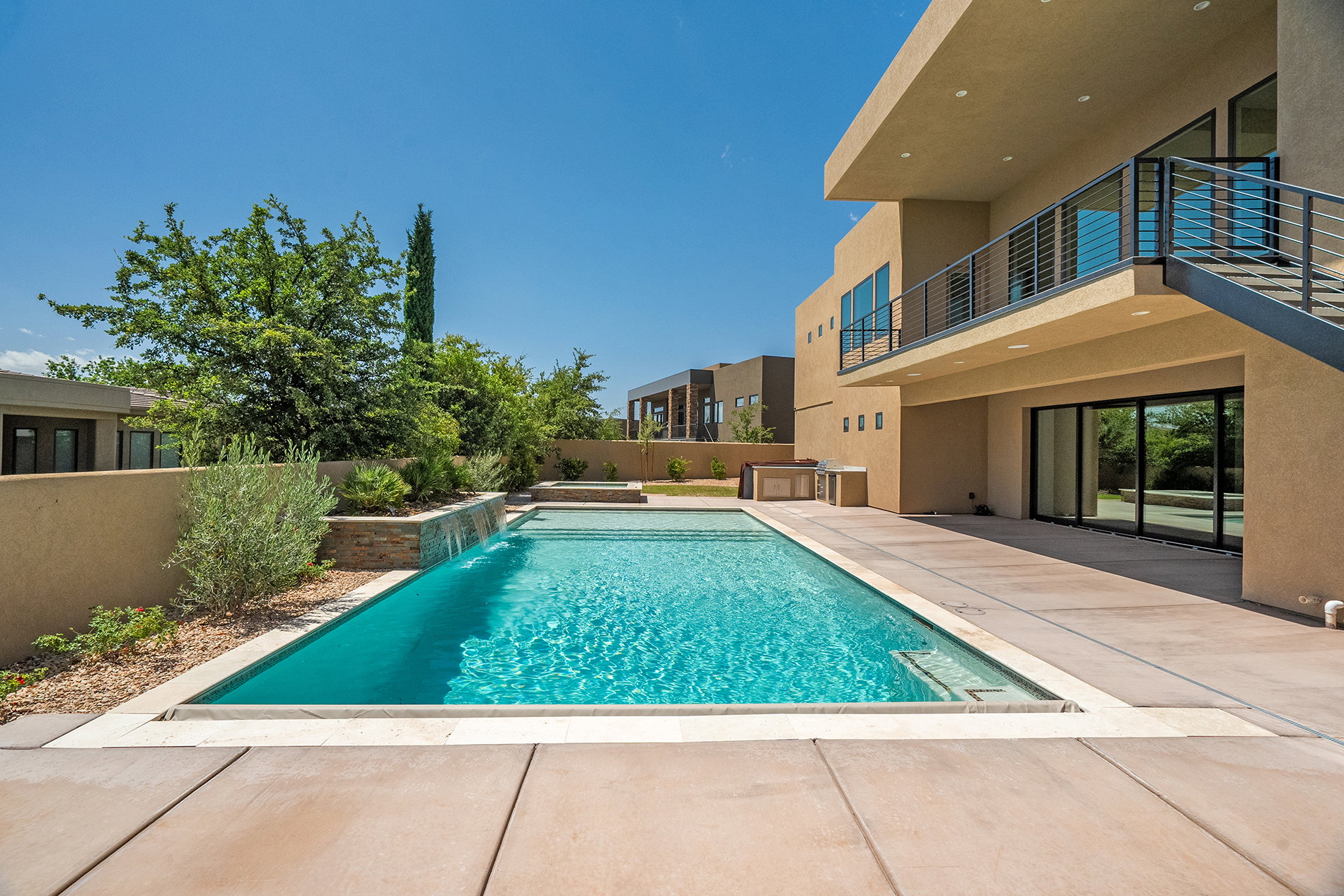 Modern stucco exterior with an outdoor pool, a water feature, a large patio, and an outdoor kitchen area