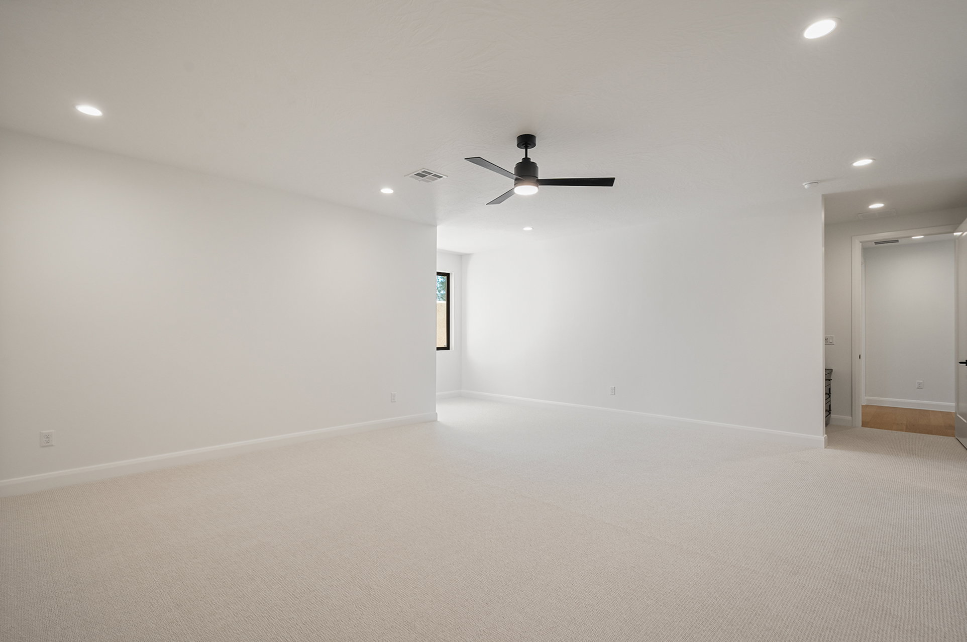 Spacious room featuring light-toned carpeting, recessed ceiling lighting, a modern ceiling fan, and white baseboards