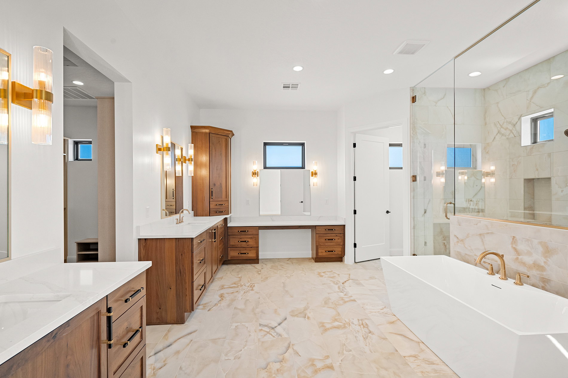 Spacious bathroom featuring expansive wood-finish cabinetry, white countertops, and a built-in soaking tub with gold-finish fixtures