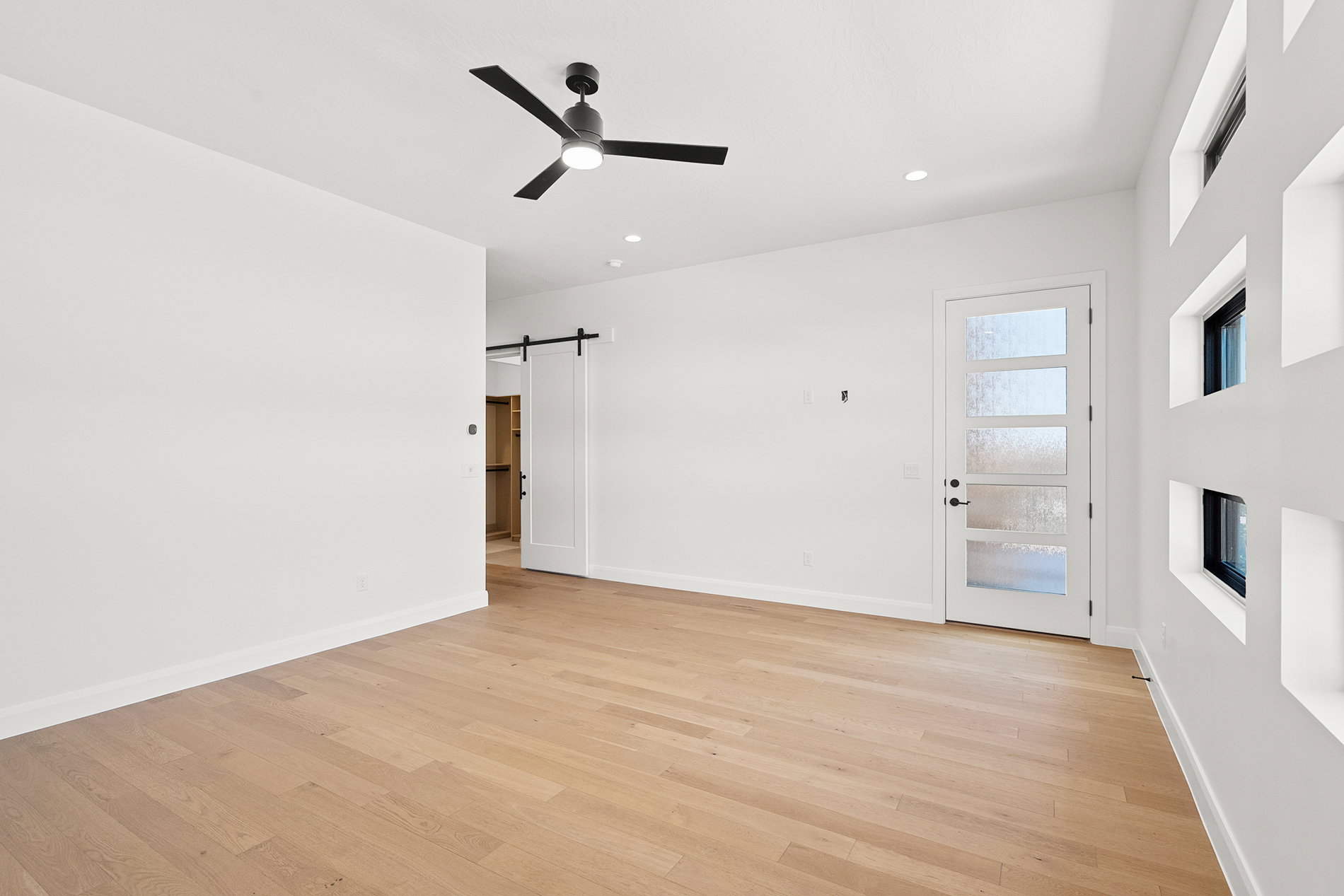 Spacious room featuring wood-finish flooring, a contemporary ceiling fan, recessed lighting, and a white barn door