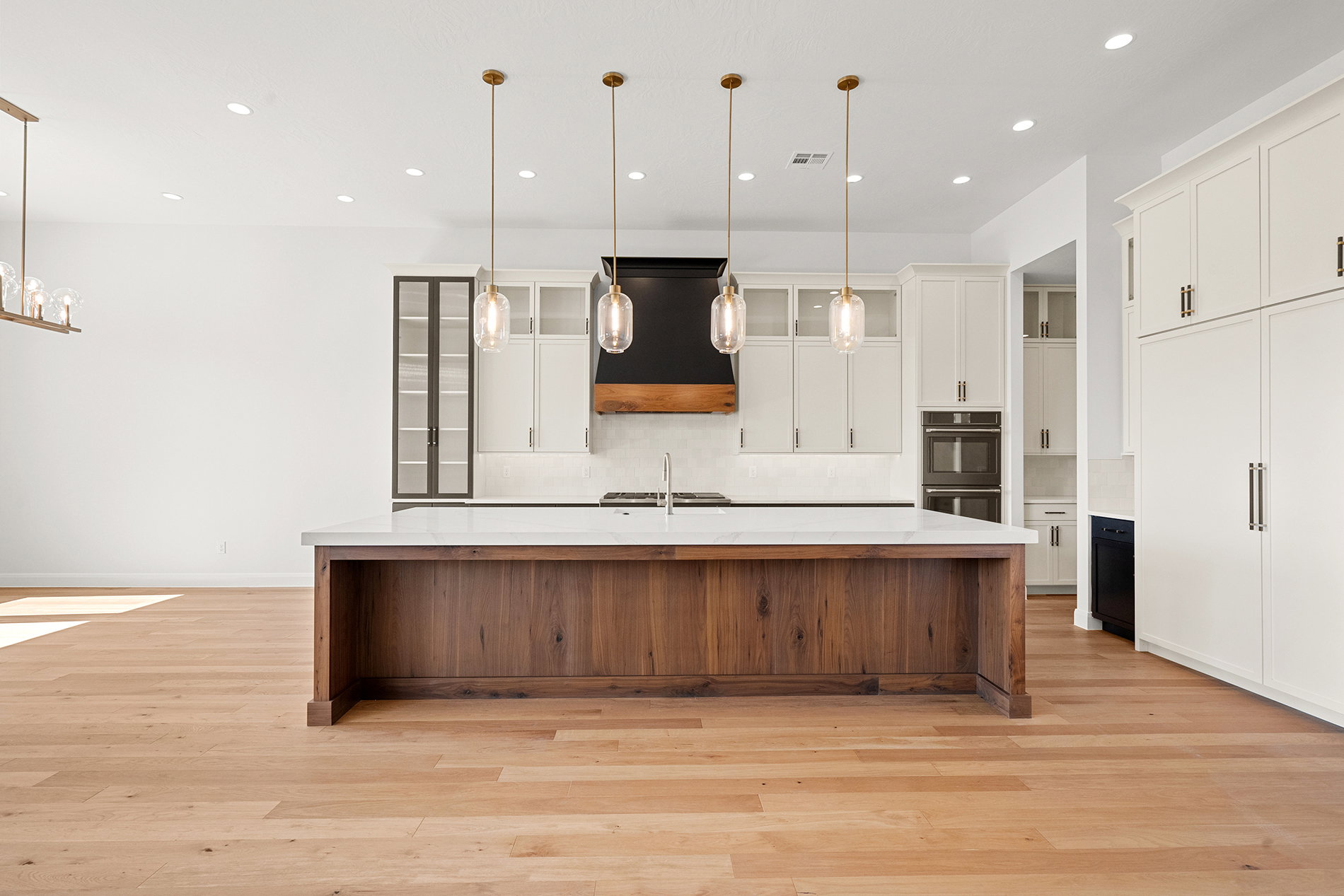Kitchen featuring a large wood-finish island with a light-toned countertop, four pendant lights, white cabinetry, and built-in double ovens