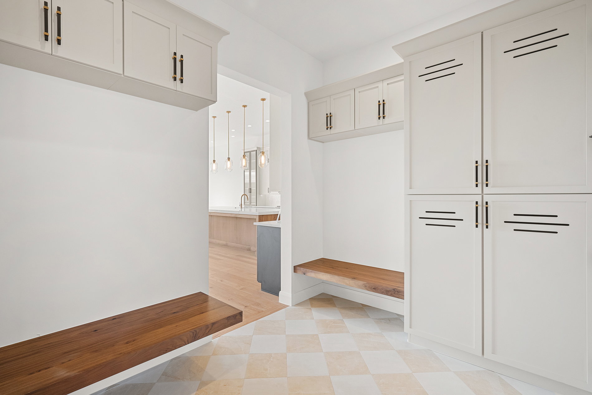 Mudroom featuring light-colored cabinetry with dark hardware, built-in wooden benches, and checkered floor tiling