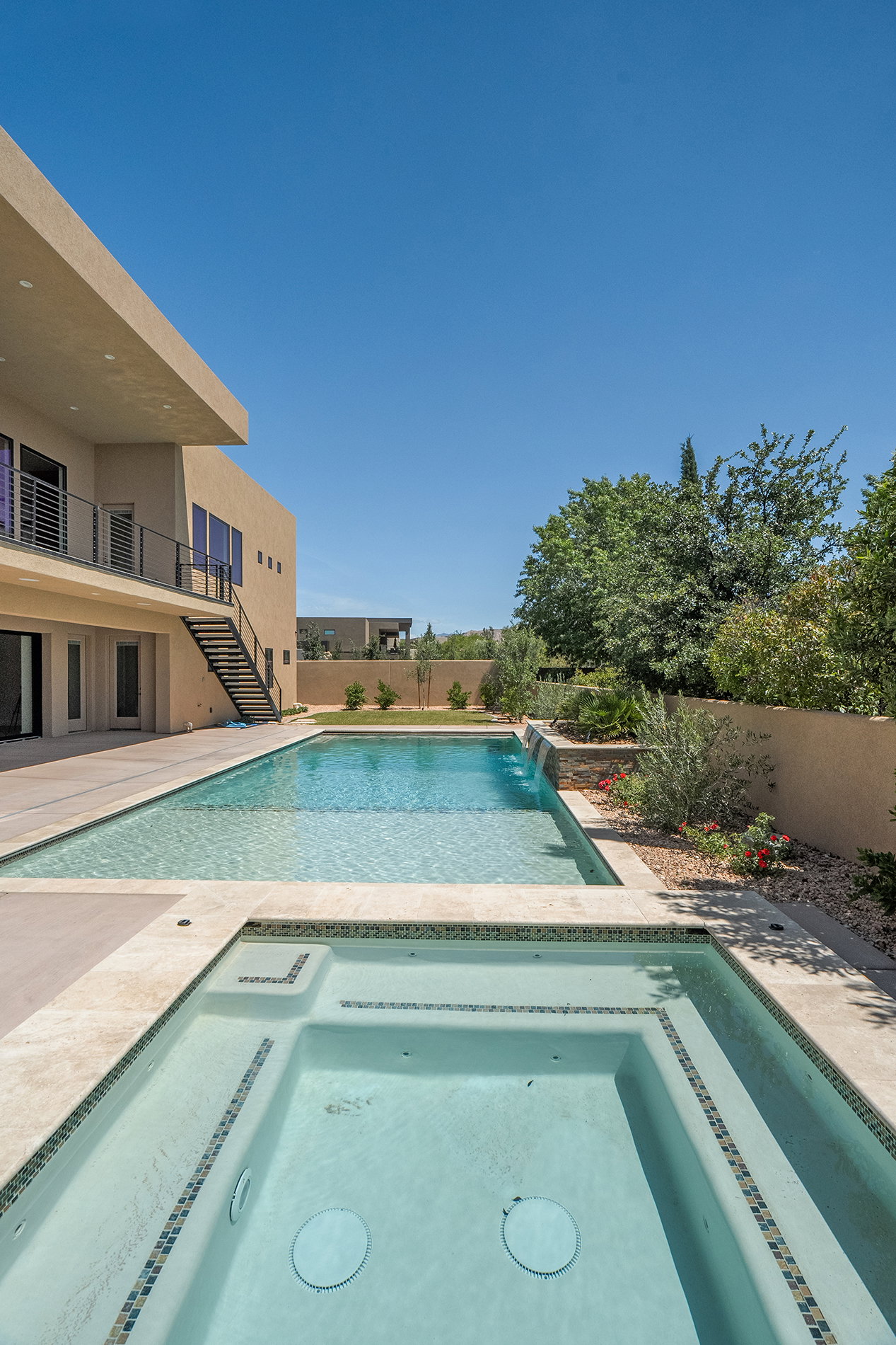 Outdoor living area featuring a rectangular swimming pool, integrated spa with mosaic tile accents, and a tiered water feature
