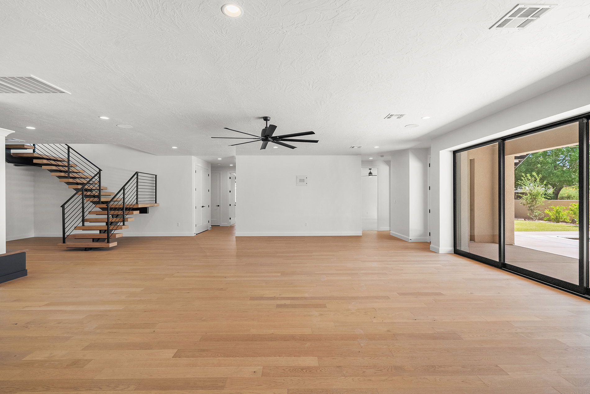 Spacious interior featuring wide plank wood-finish flooring, a modern open-tread staircase with black metal railing, and large sliding glass doors opening to the exterior