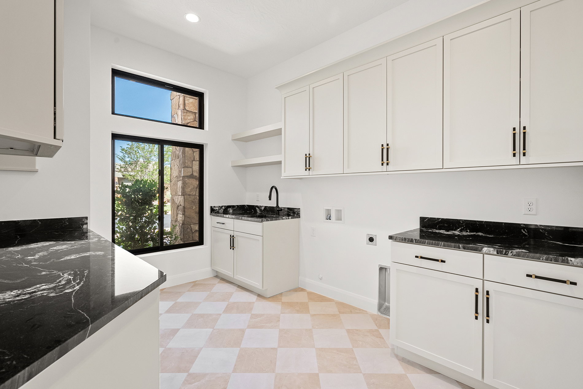 White shaker cabinetry with black hardware, dark stone countertops, checkered tile flooring, and integrated wall shelving