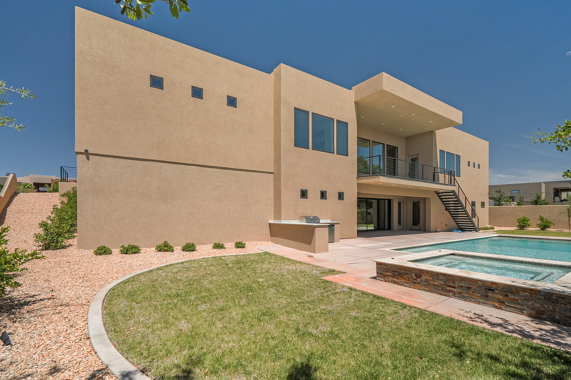 Contemporary stucco exterior featuring a built-in outdoor grill, a rectangular swimming pool, and an integrated spa with stone veneer surround