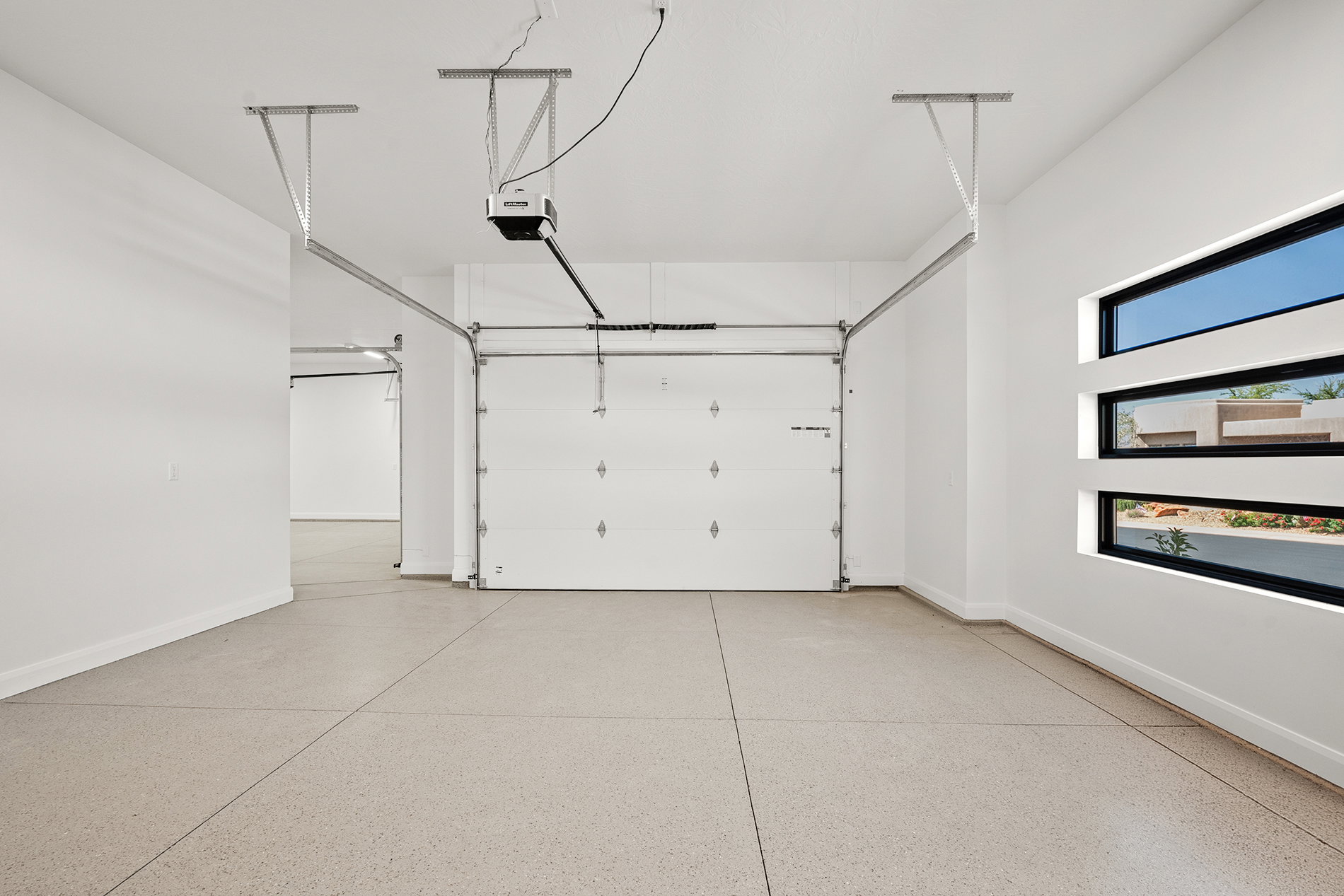 Spacious garage featuring light-colored epoxy flooring, an automatic garage door opener, and a white paneled garage door