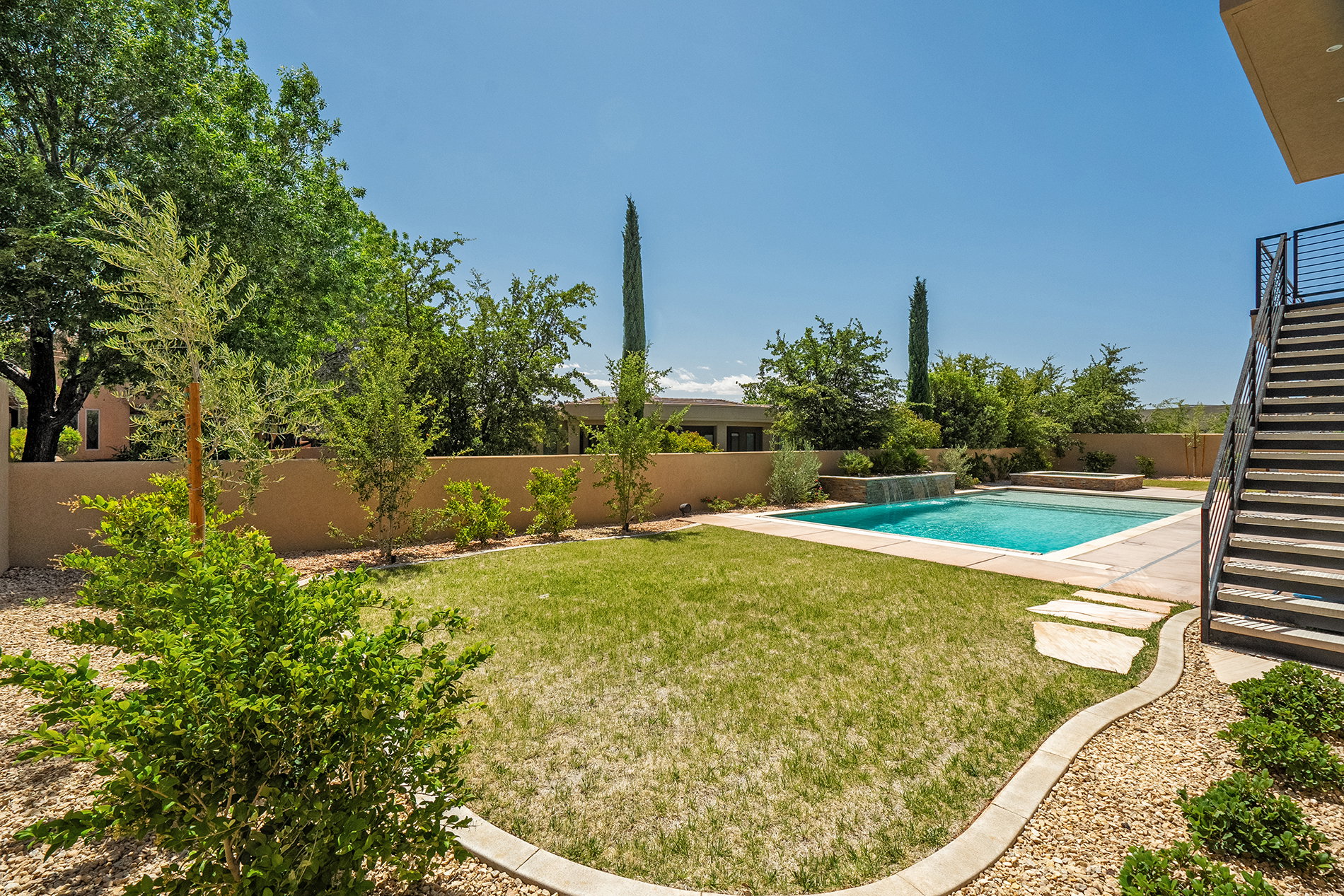 Expansive backyard featuring a rectangular swimming pool with a waterfall feature, a surrounding concrete patio, and a manicured lawn area