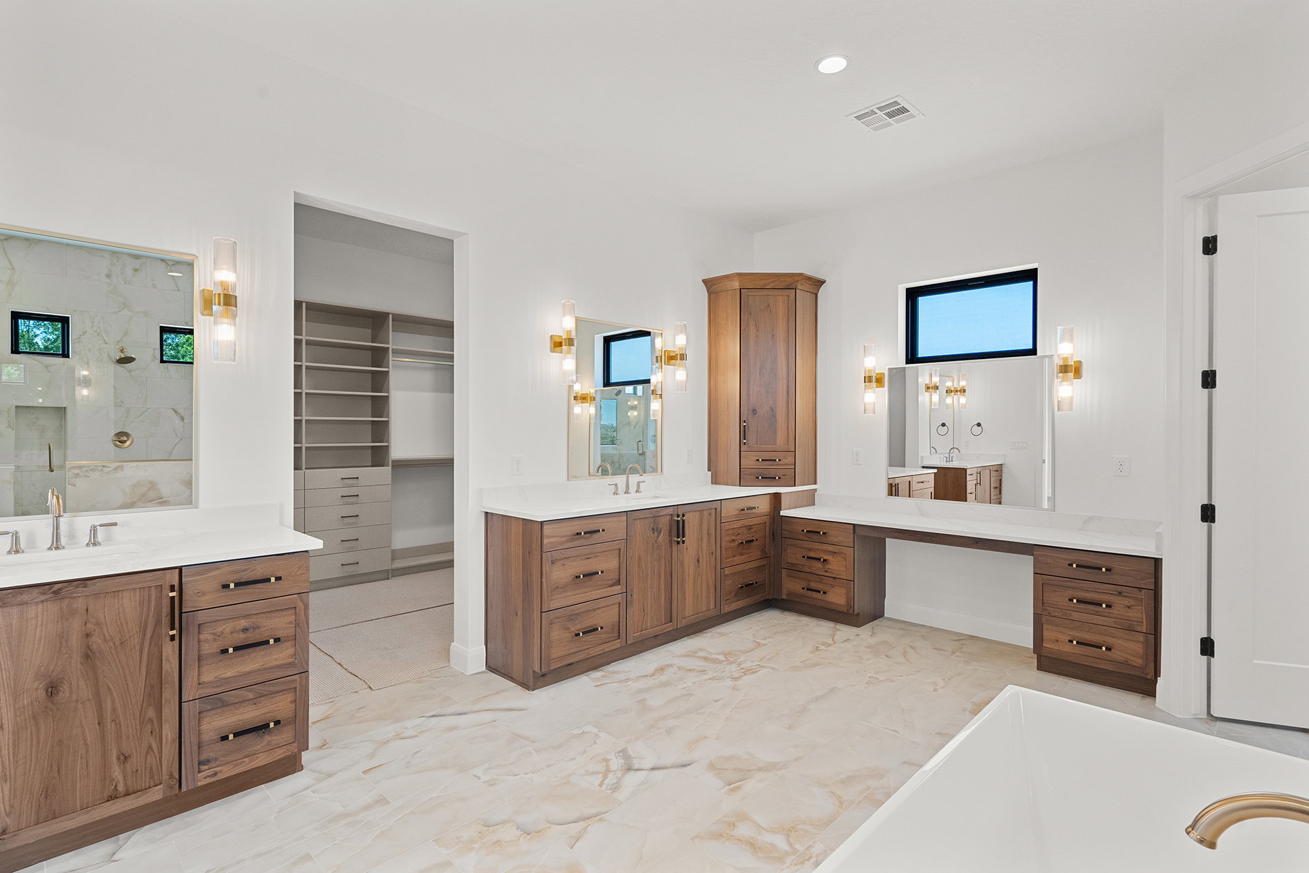 Spacious bathroom featuring two wood-finish vanities with undermount sinks, white countertops, and wall-mounted sconces