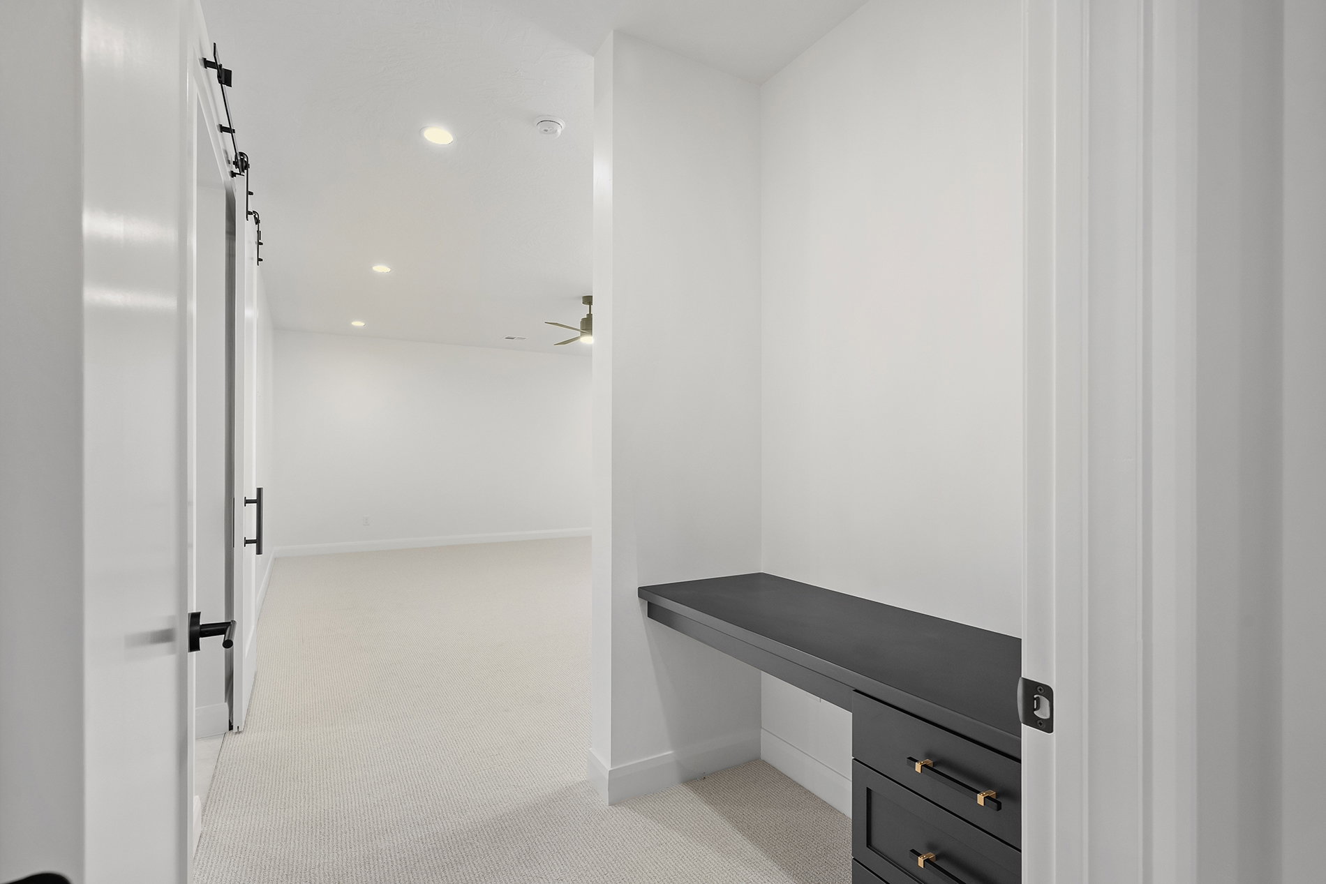 Built-in black desk with integrated drawers, black door hardware, recessed lighting, and a ceiling fan