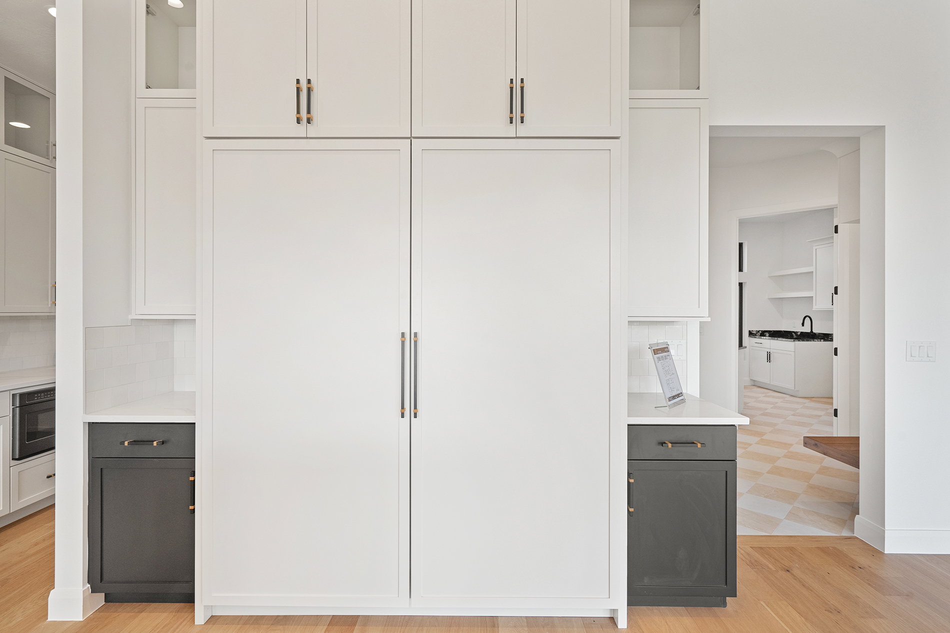 Integrated panel-ready refrigerators flanked by white upper cabinetry with brass hardware