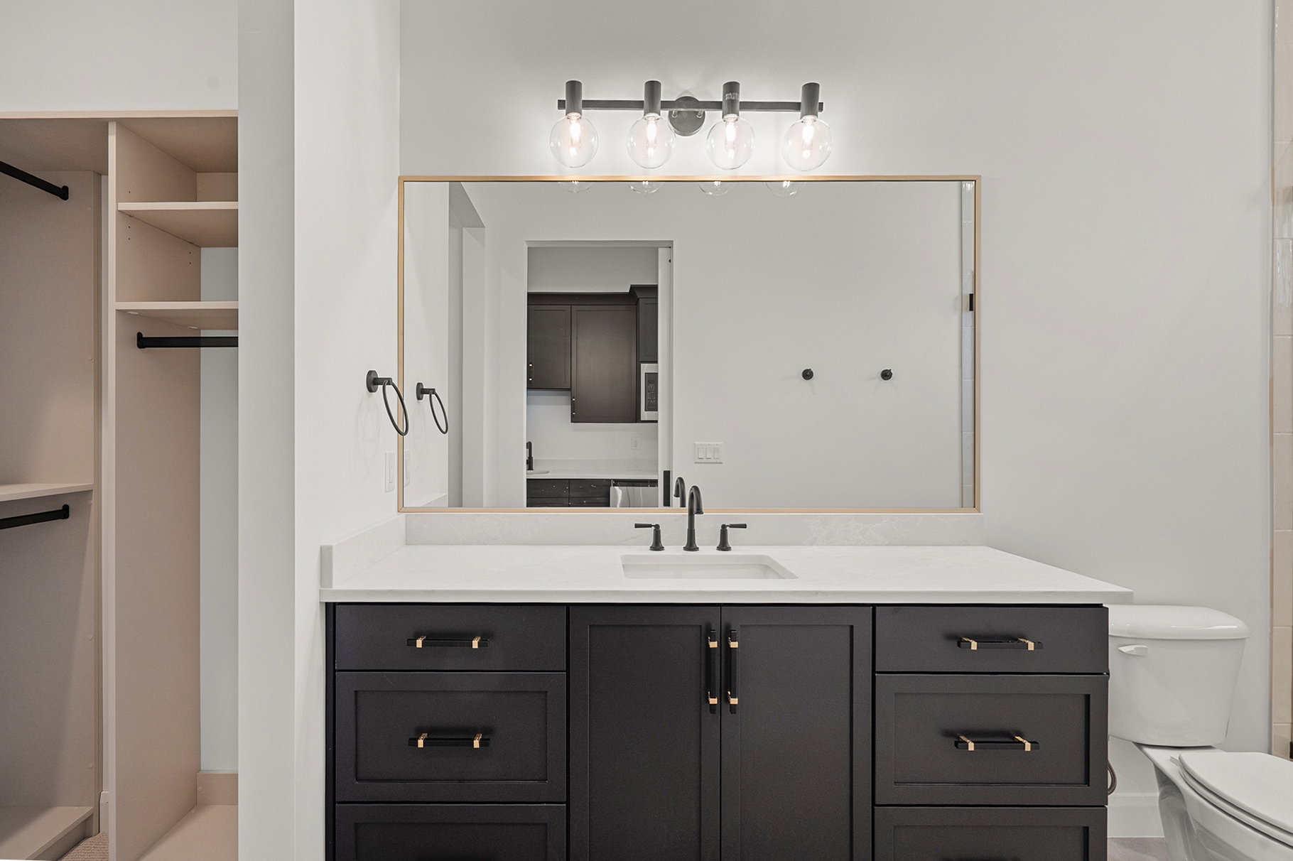 Bathroom vanity featuring a quartz countertop, integrated sink, matte black faucet, and dark cabinetry with gold-tone hardware