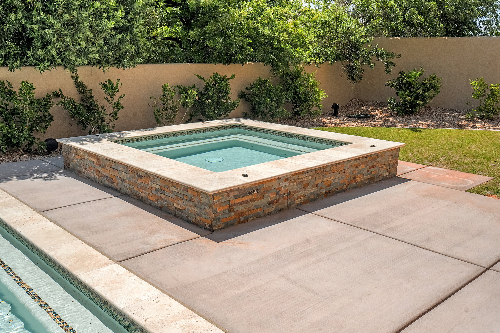 Built-in spa with stone veneer surround and tile coping, situated on concrete hardscaping