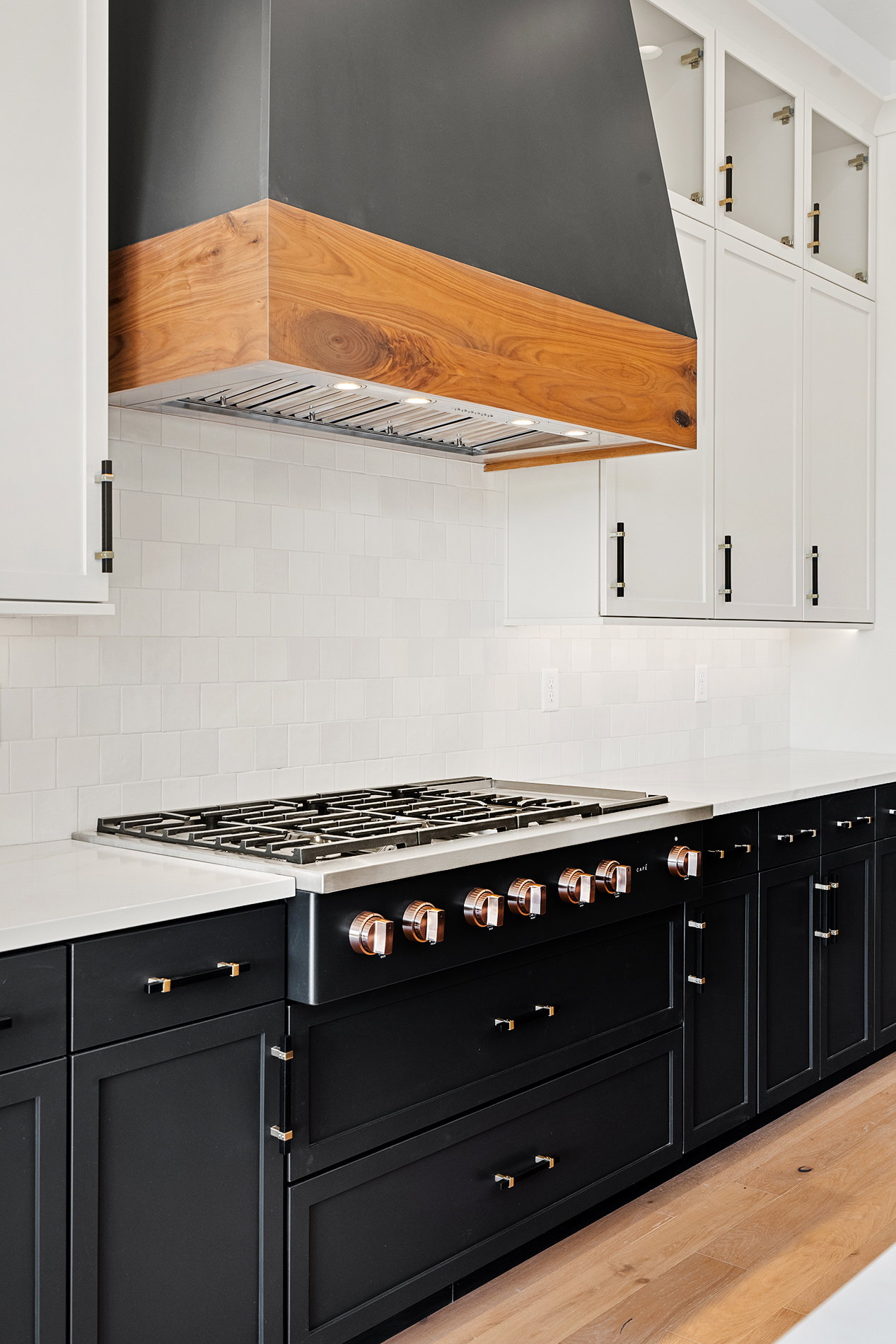 Gourmet kitchen featuring a wood-accented range hood, professional-grade gas range with copper-toned hardware, white subway tile backsplash, and contrasting black and white cabinetry with gold-toned hardware