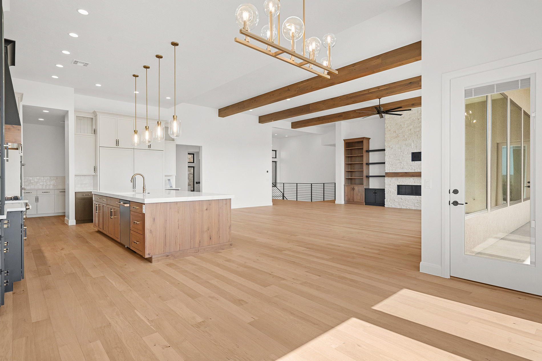 Open-concept living area featuring light wood-finish flooring, exposed ceiling beams, and recessed lighting