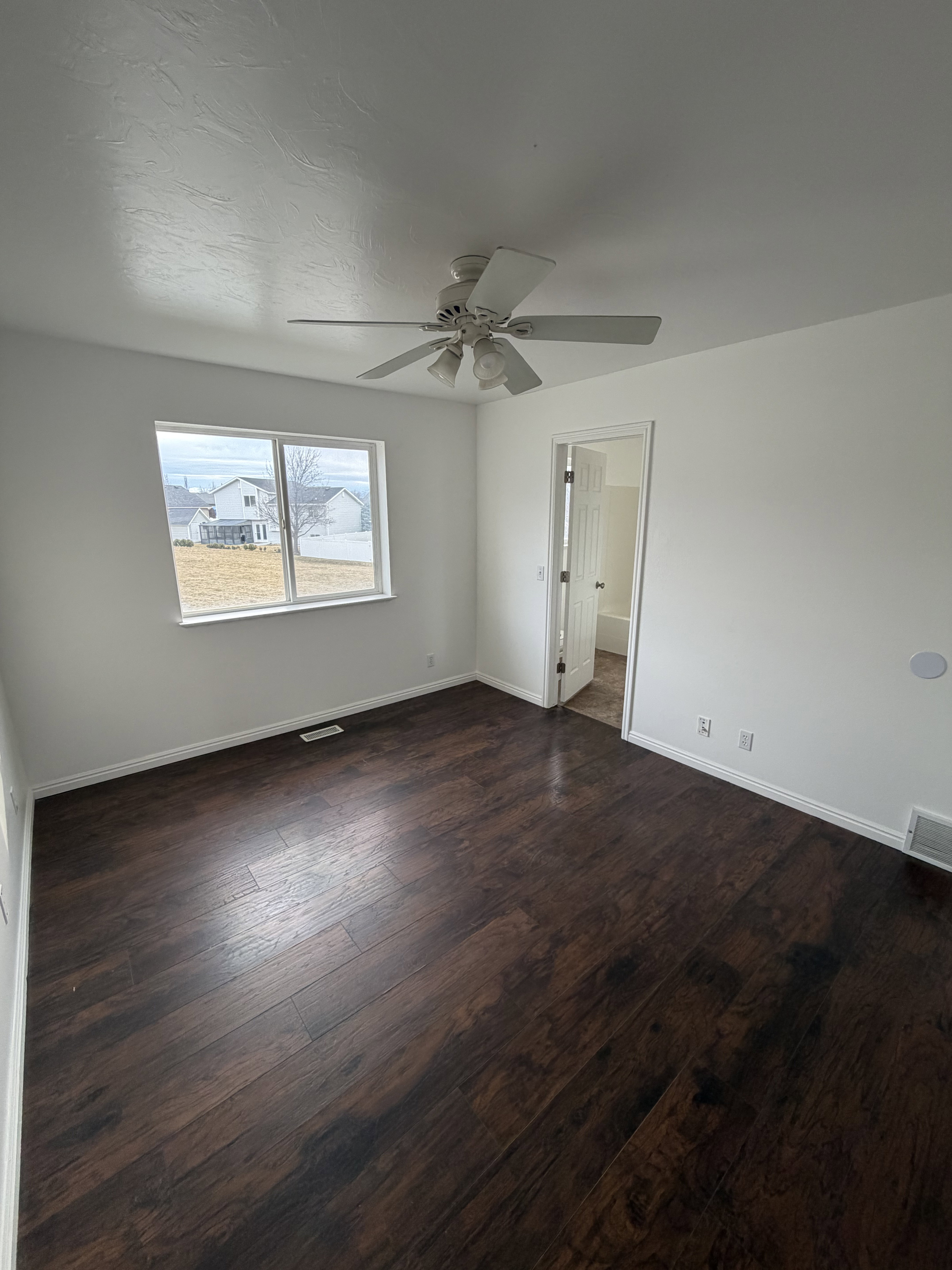 Spacious room featuring dark wood-finish flooring, white baseboards, and a contemporary ceiling fan