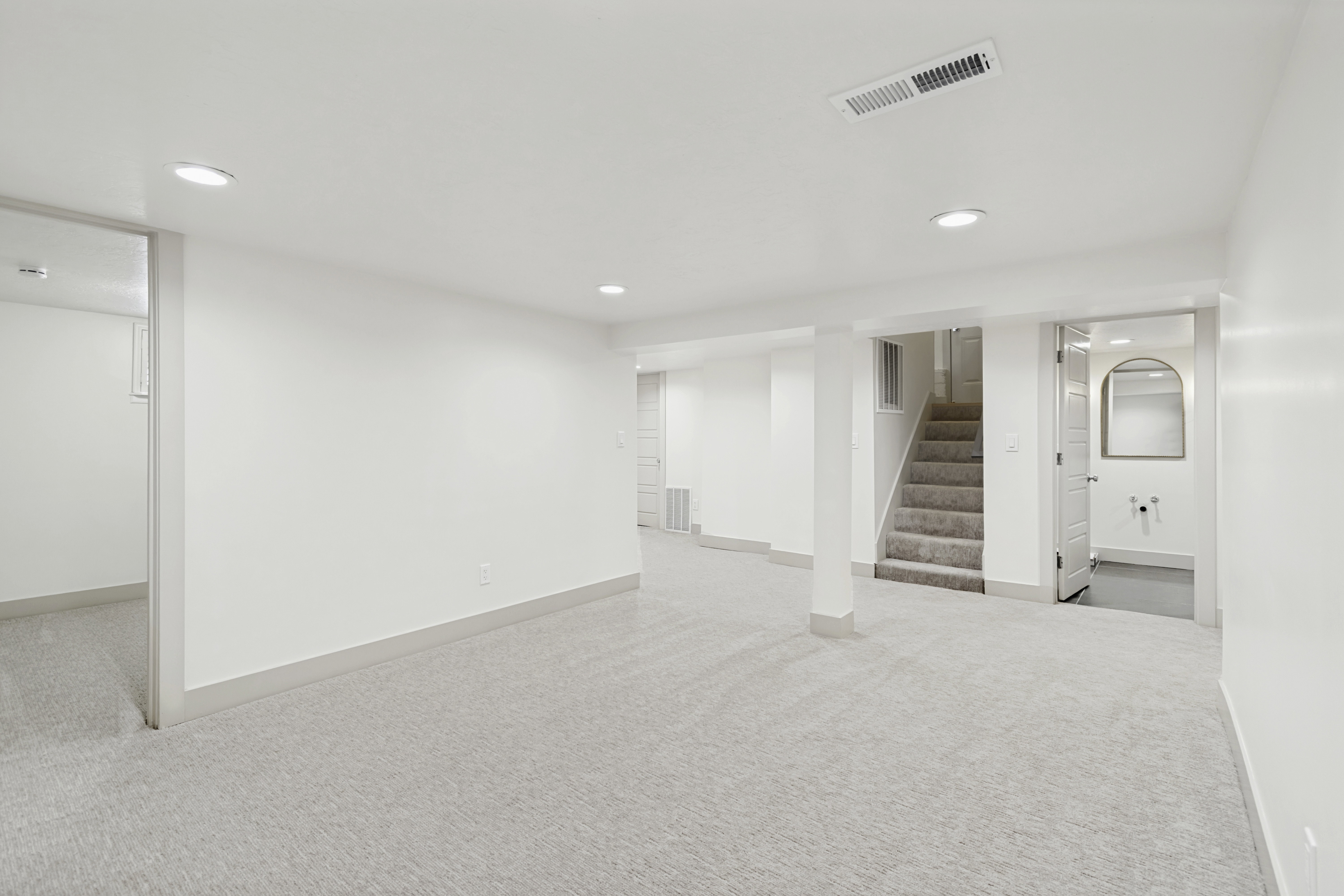 Spacious lower level featuring light-colored carpeting, recessed lighting, painted white walls, and a visible staircase with carpeted treads