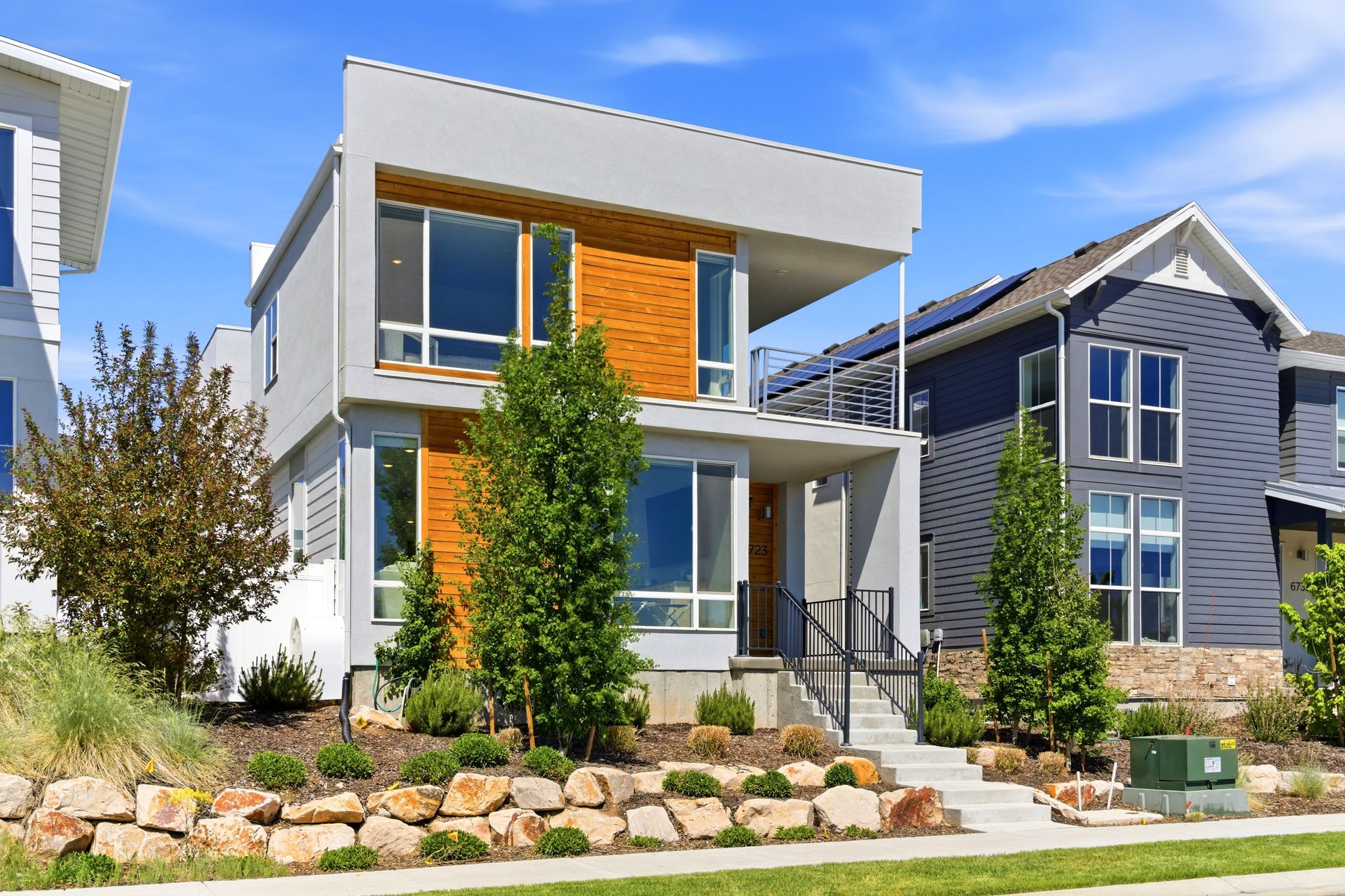 Modern exterior featuring a flat roofline, horizontal wood-finish siding, and a second-story balcony with metal railings